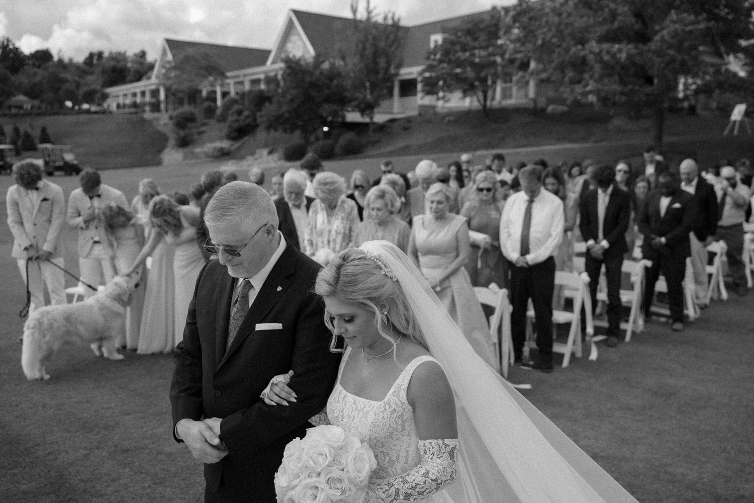 Black and white panoramic of outdoor wedding ceremony with guests seated on lawn.