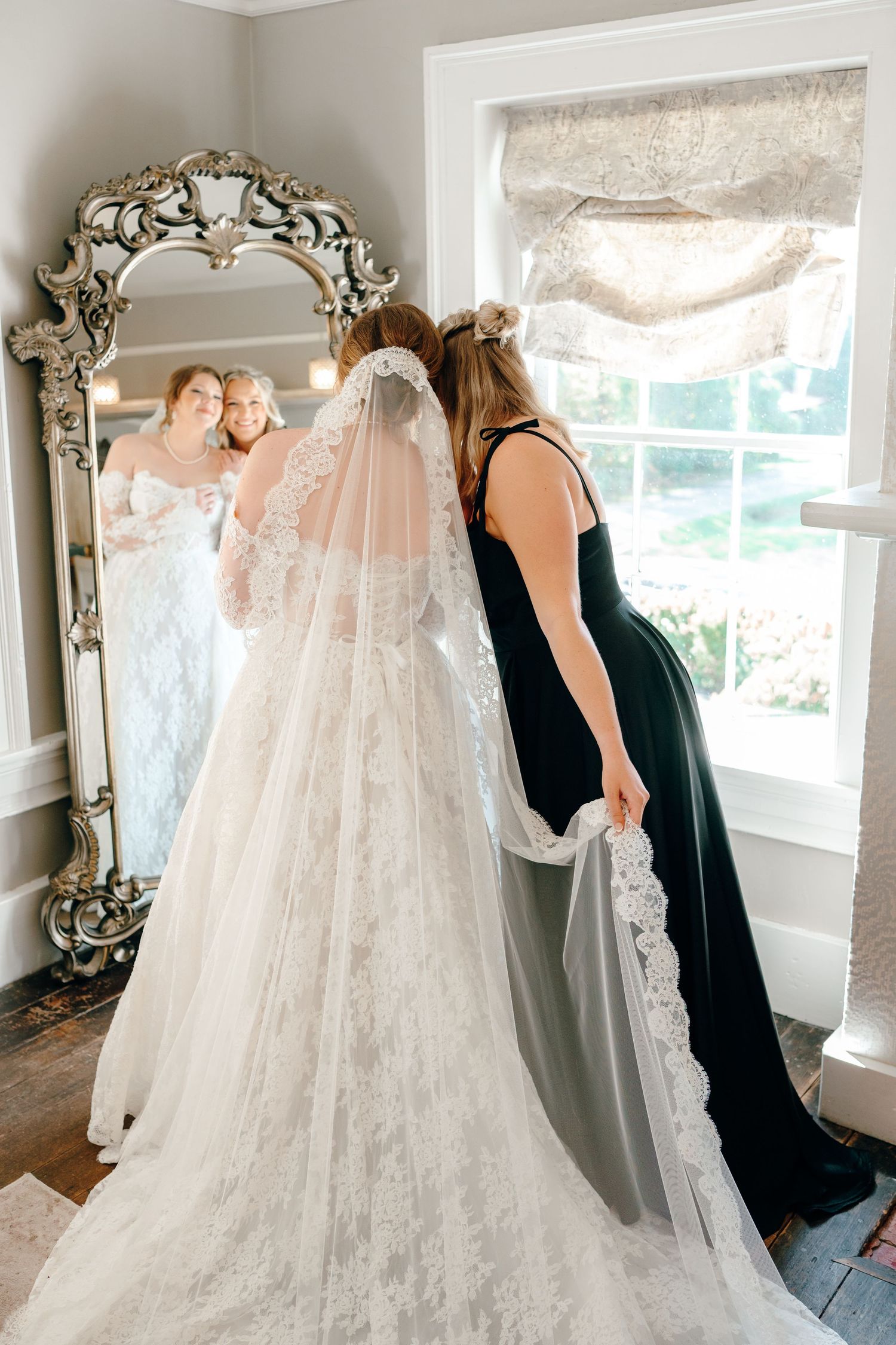 Intricate lace wedding gown being prepared in bridal suite with elegant mirror.
