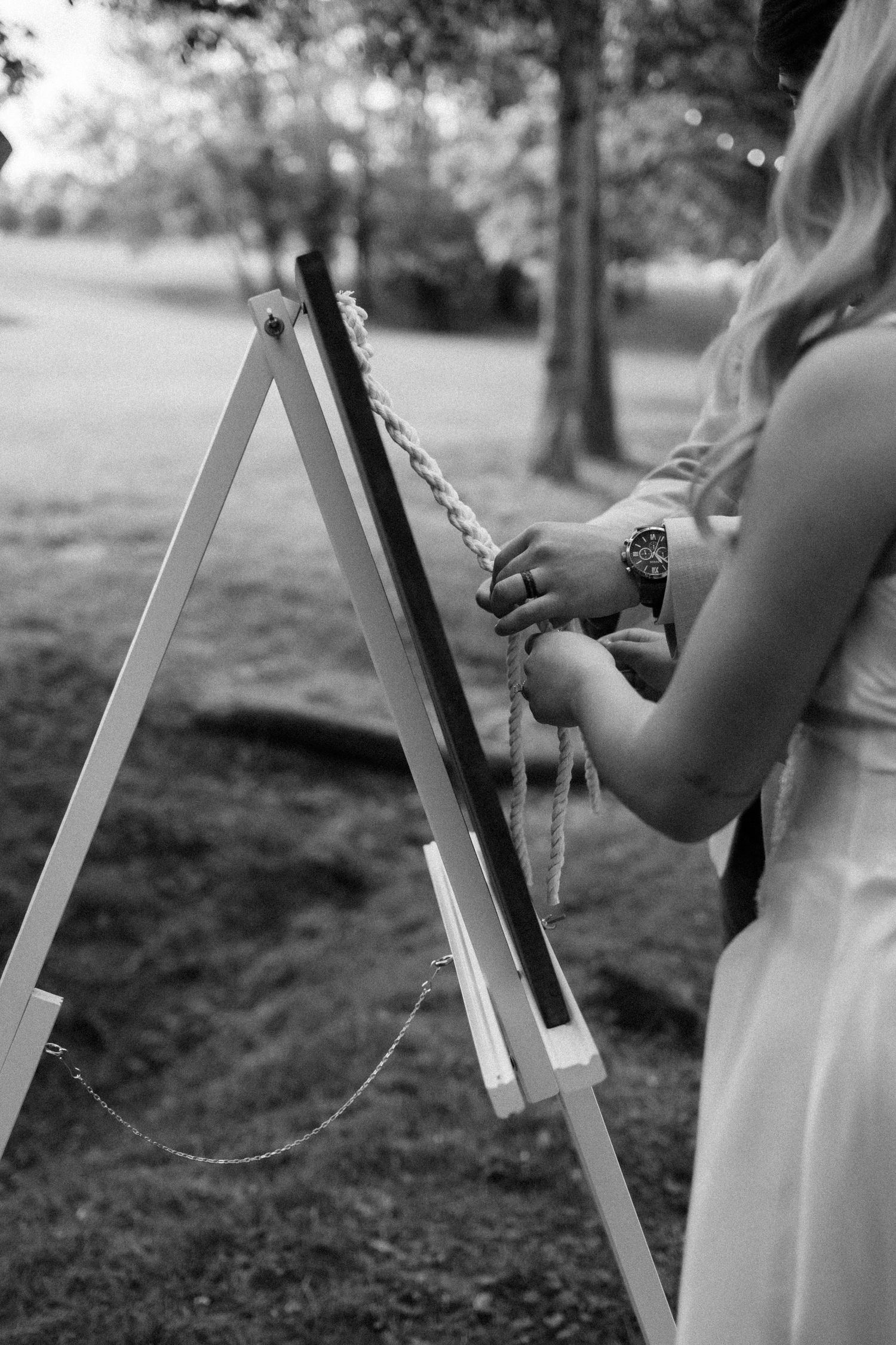 Close-up of hands writing on easel at outdoor wedding setting in black and white.
