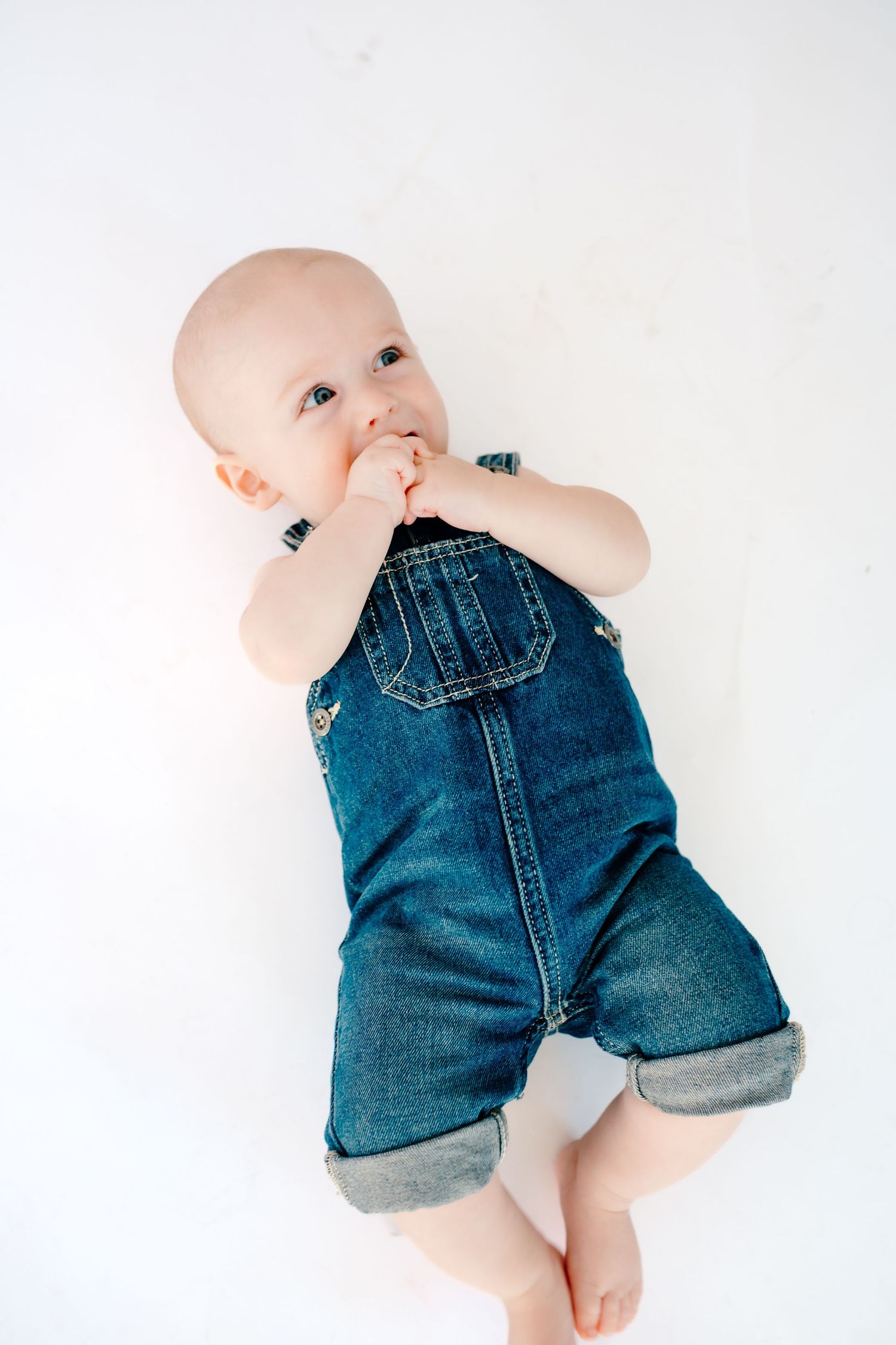 Baby wearing denim overalls lies on white background in sequence showing different playful poses.