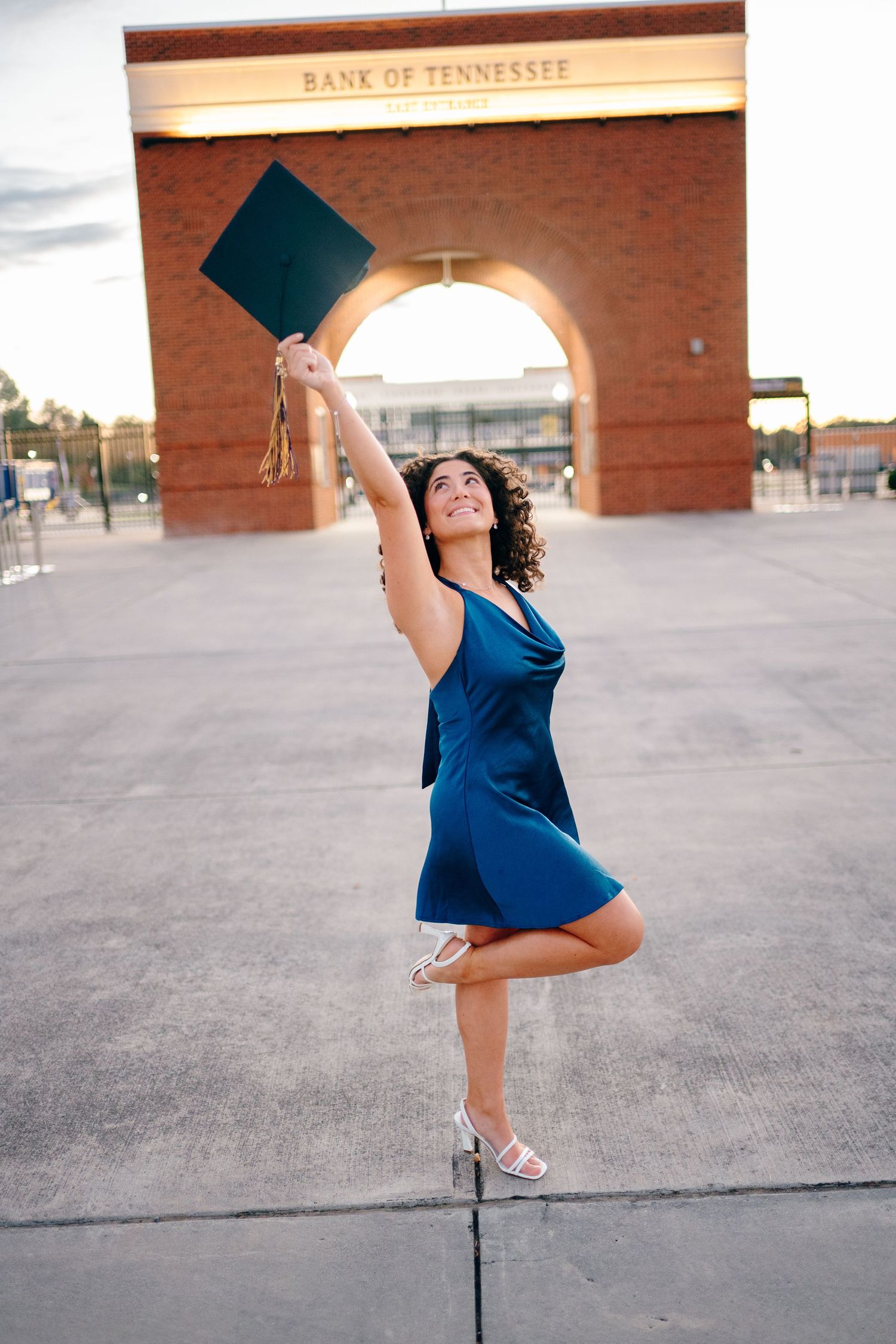 Graduate celebrates by tossing cap in front of Bank of Tennessee building.