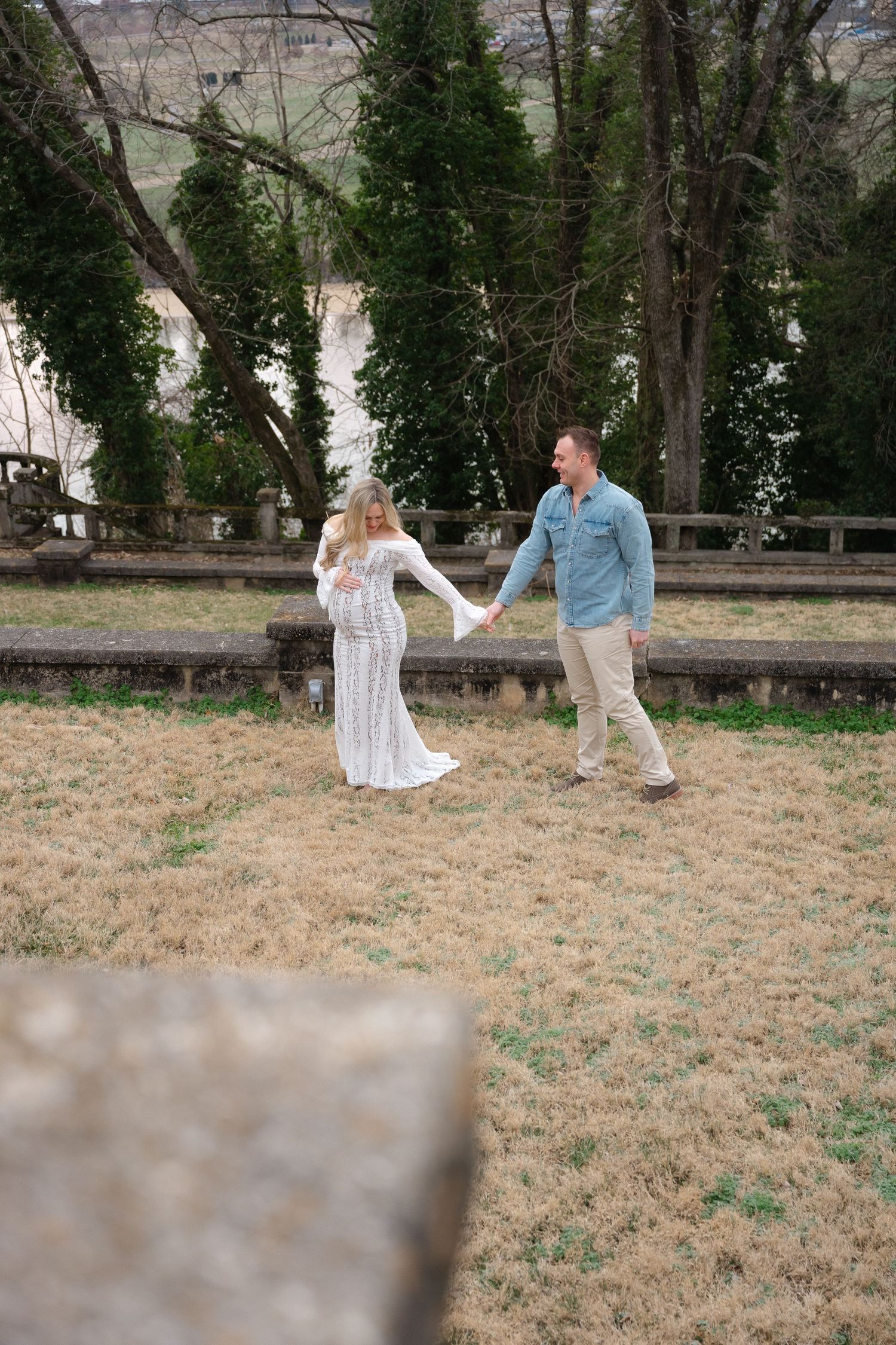 Couple walking and posing in outdoor field during maternity photoshoot.