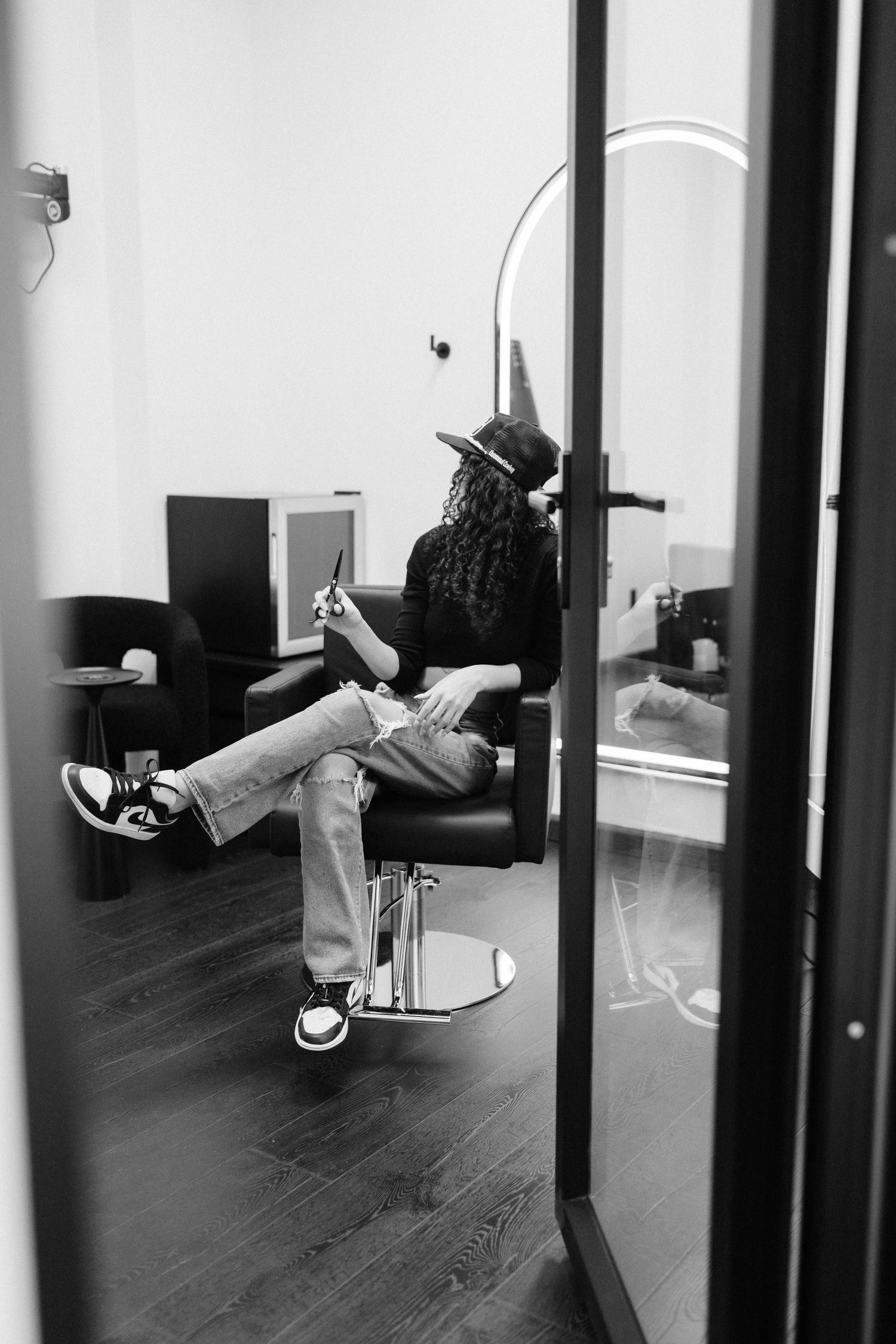Black and white photo of someone relaxing in a salon chair wearing casual attire and sneakers.