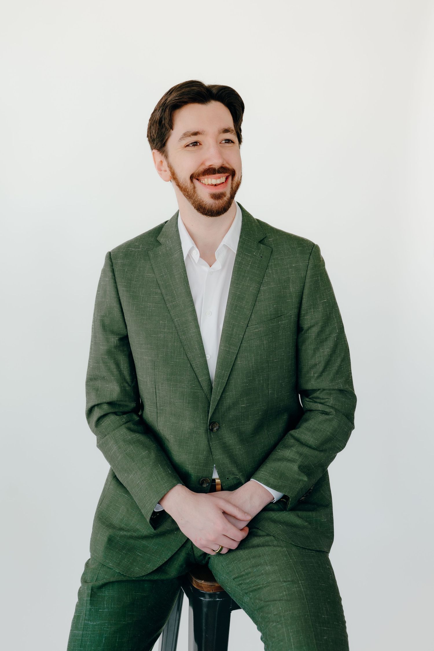 Professional wearing a green textured suit and white dress shirt smiling against white background.