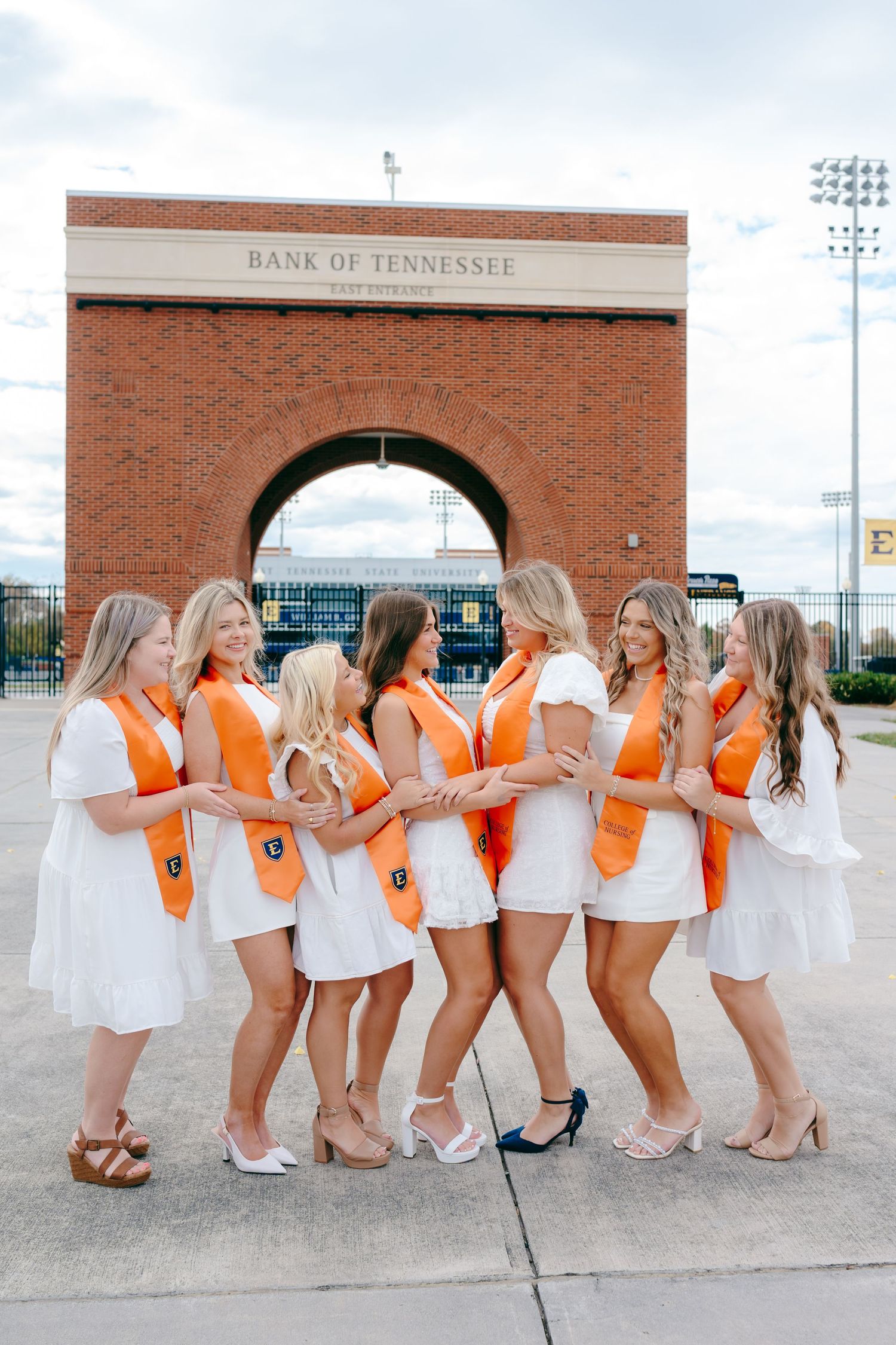 Group photo series in orange and white uniforms posing playfully against a brick stadium wall.