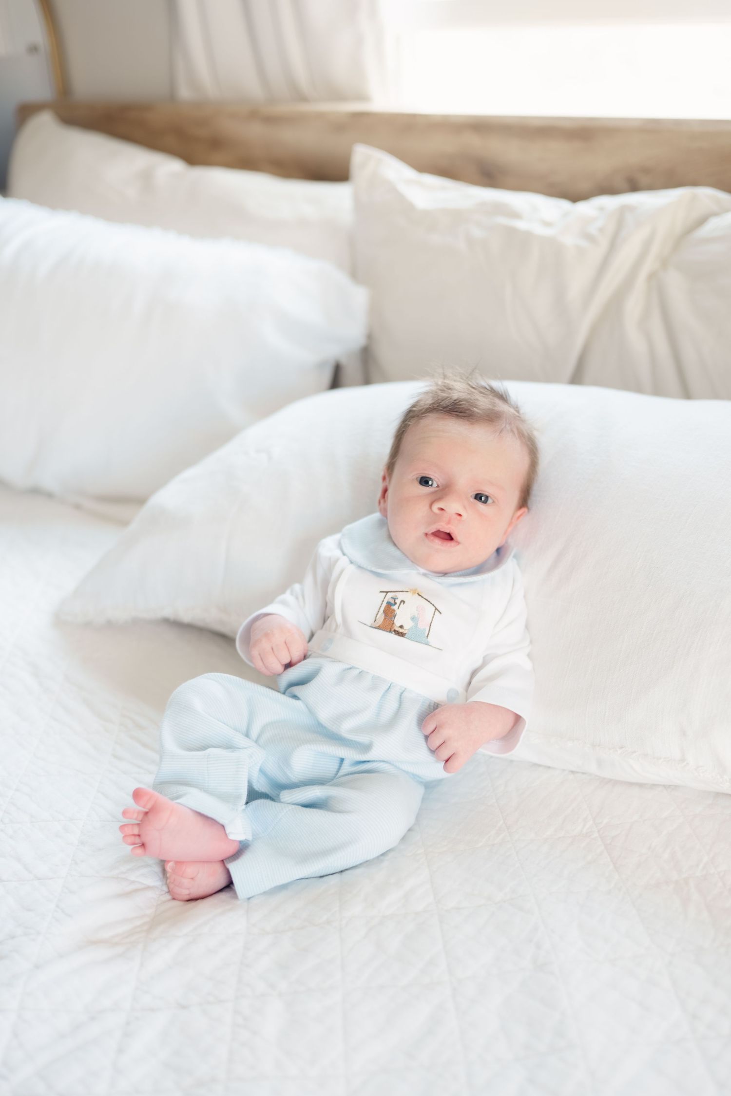 Baby in light blue onesie lying on white bedding.
