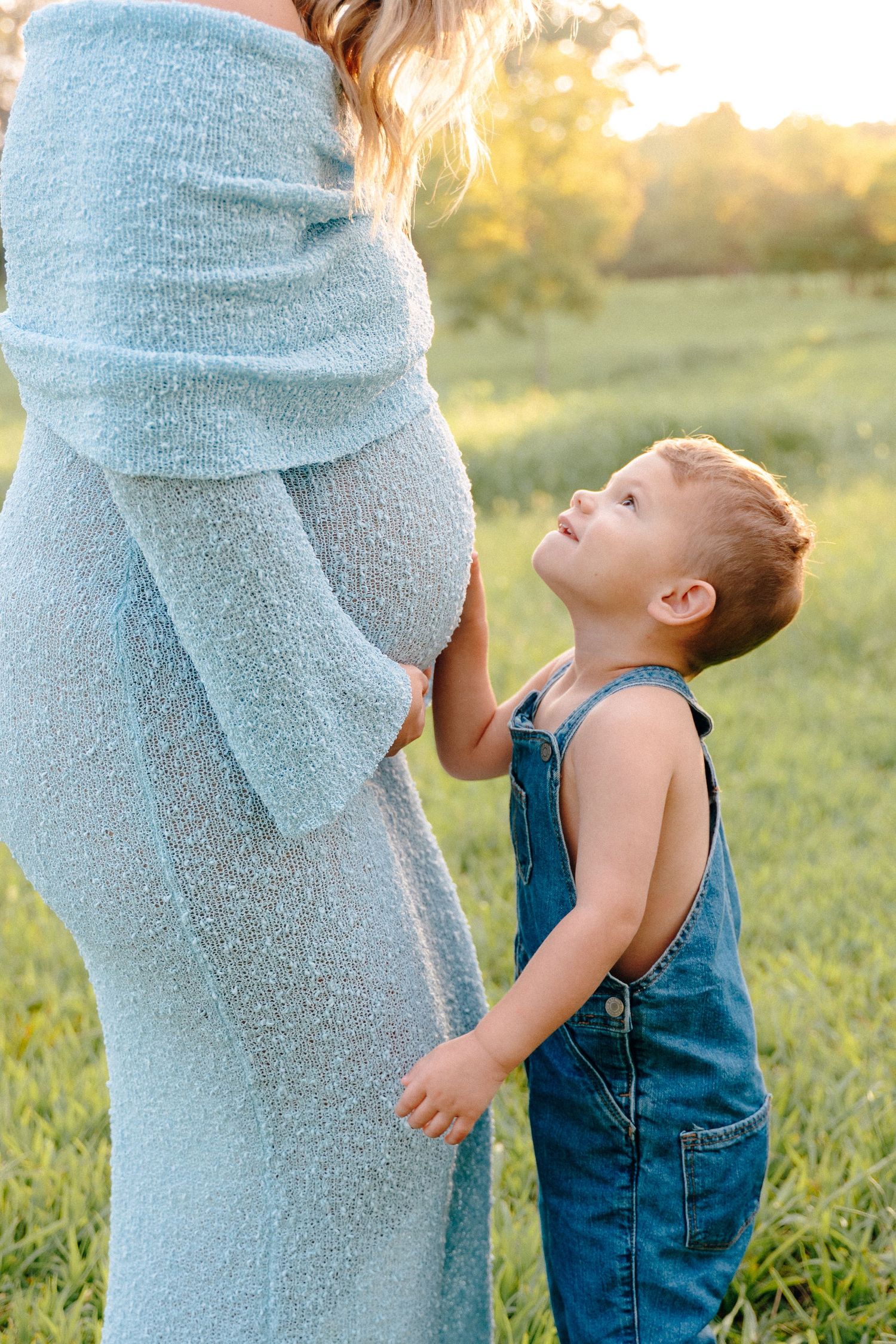 Close-up shots of a toddler interacting with a pregnant belly in a blue dress outdoors.