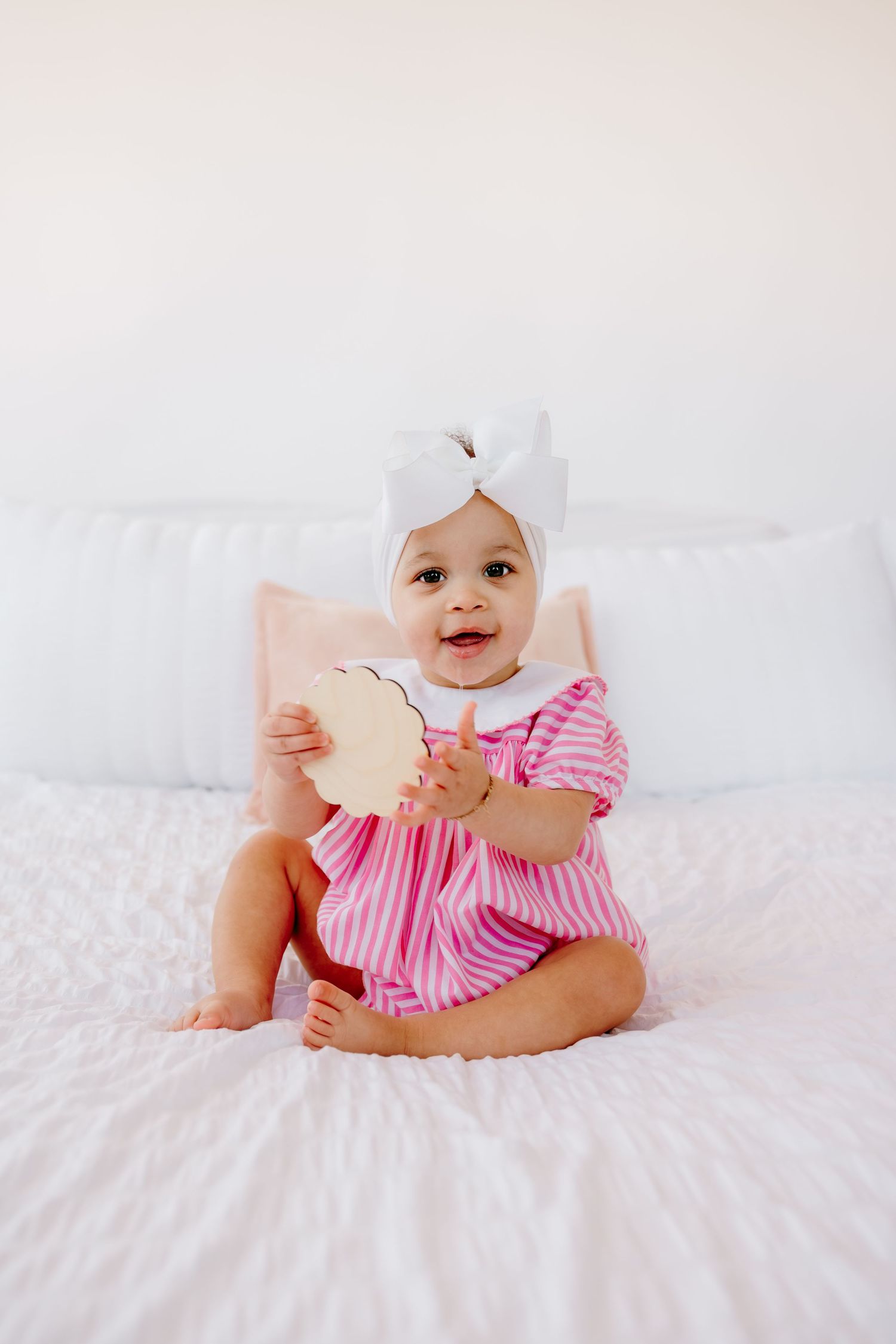 Baby in pink striped outfit lying on white bedding.