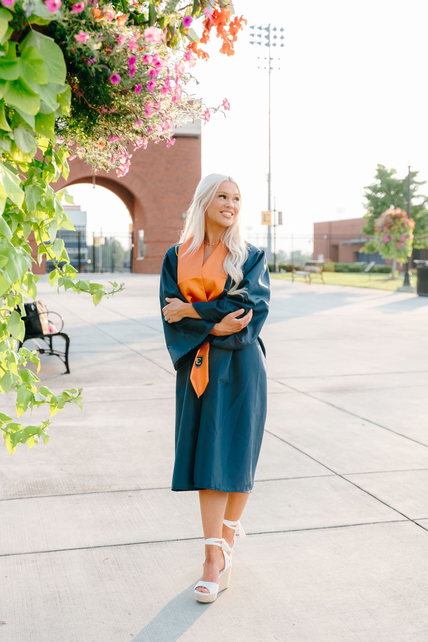 Graduation photos in navy blue gown with orange accents among blooming flowers.