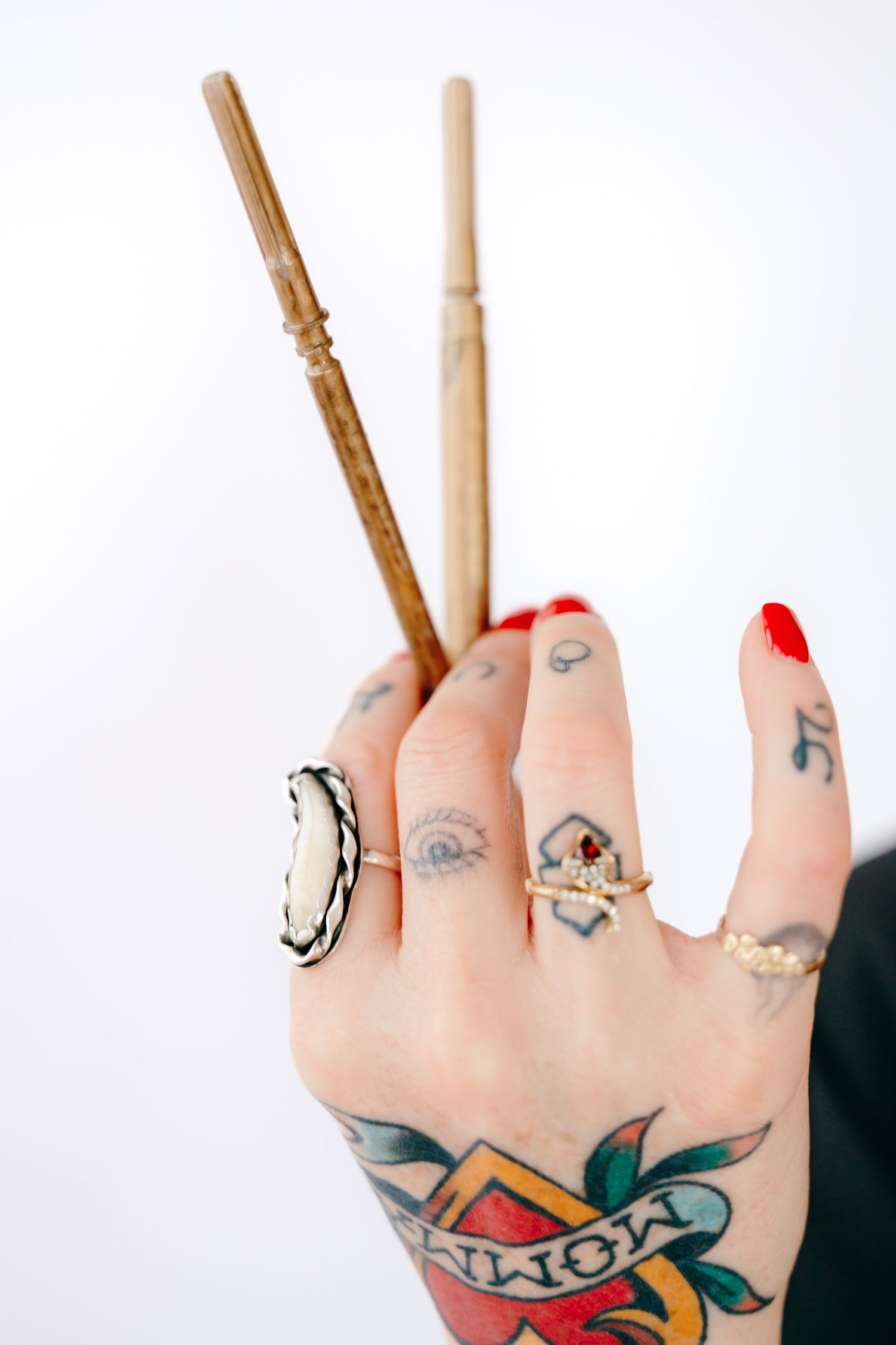 Close-up view of tattooed hands with red nail polish and multiple rings showing traditional style tattoo artwork.
