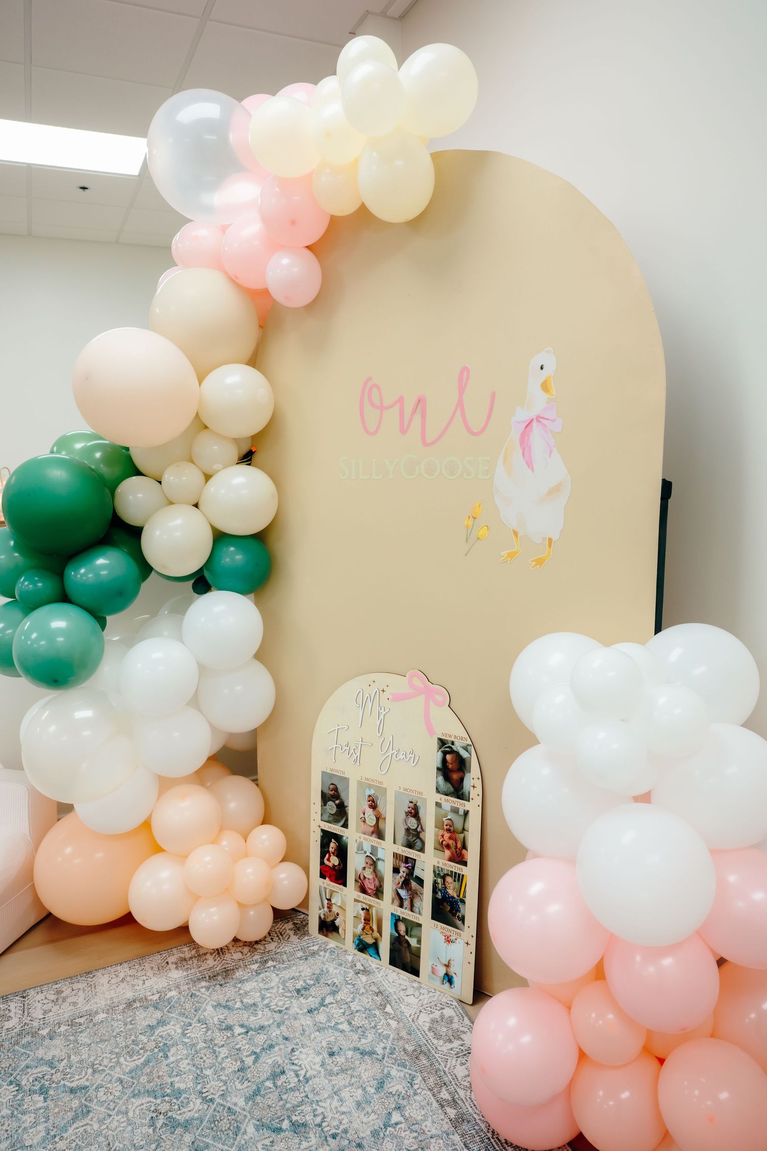Balloon arch installation in progress showing pink, white and green balloons against a beige wall with party decorations.