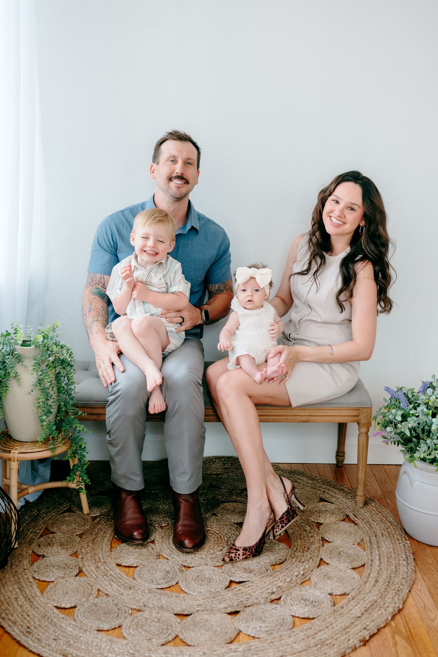 Family portrait with two small children sitting on bench surrounded by potted plants.
