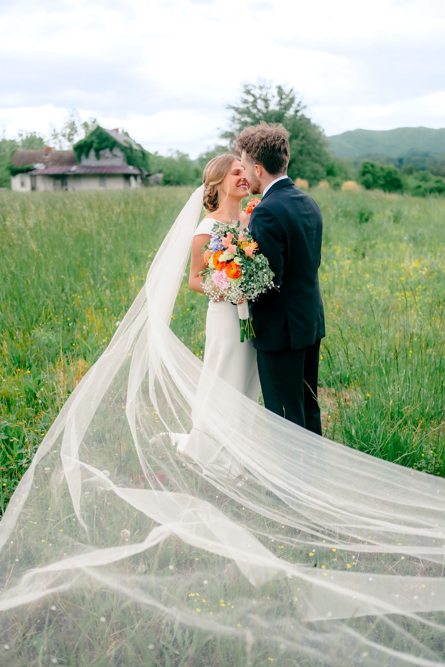 Wedding couple in field with dramatic flowing veil catching sunlight.