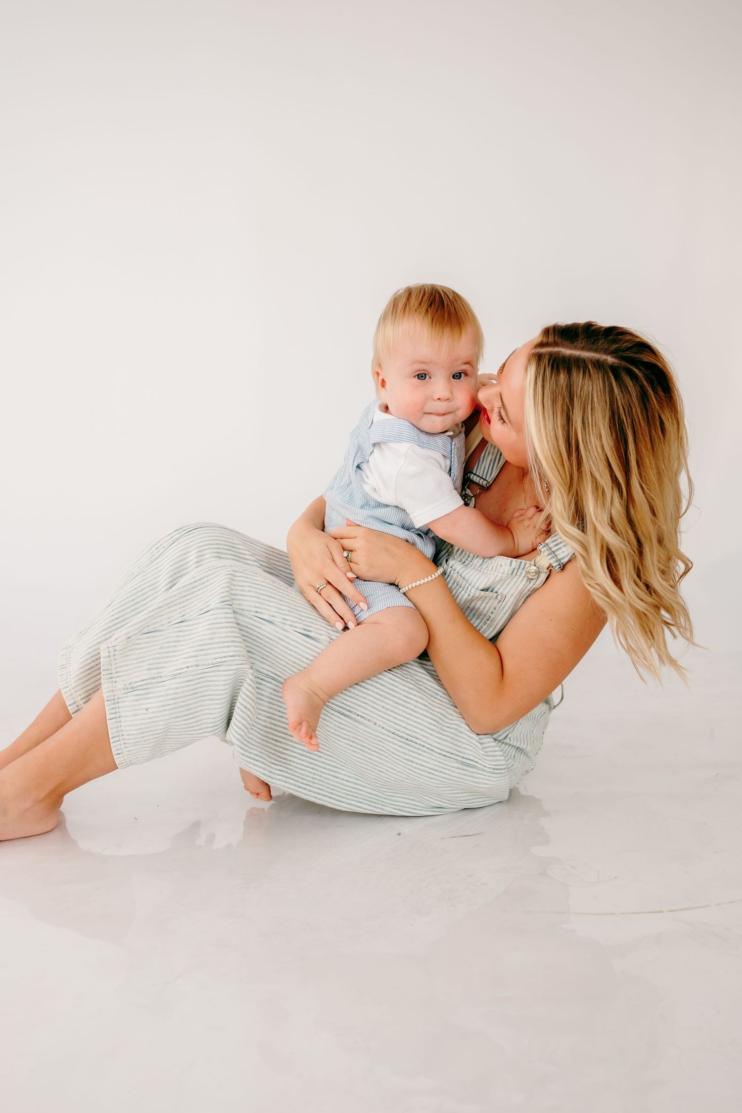 Mother and baby playing together on white floor in matching gray outfits.