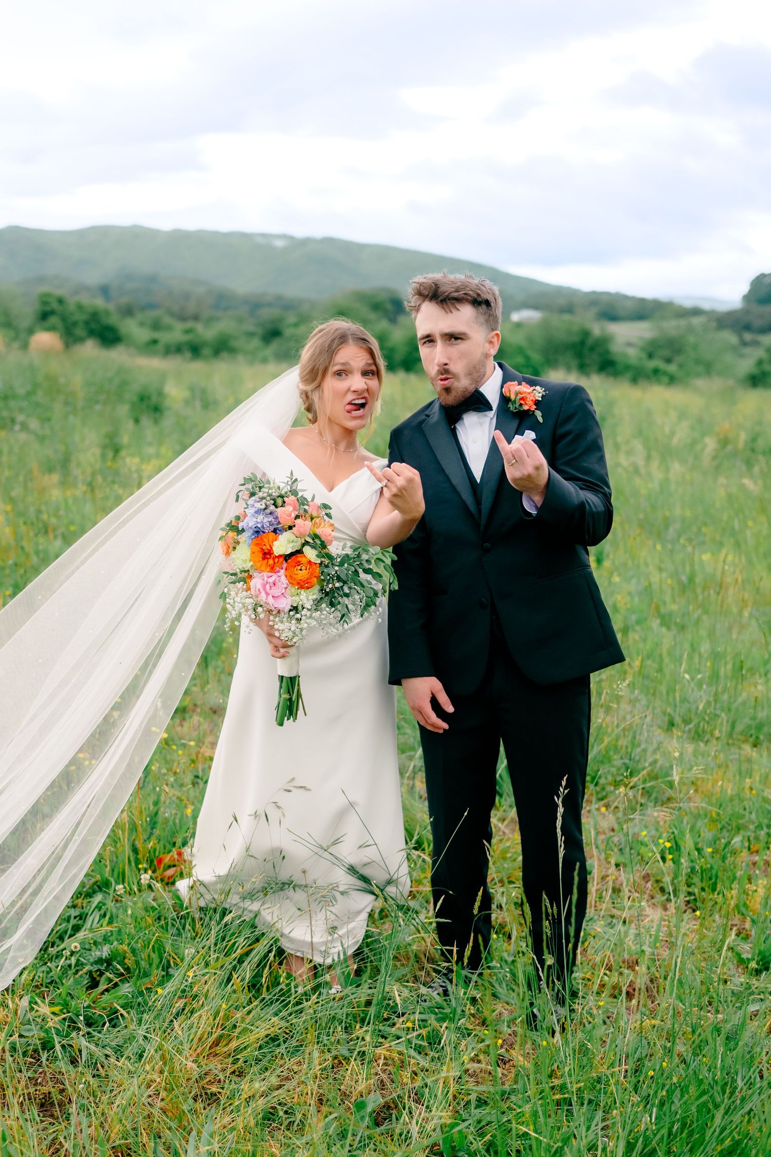 Playful wedding couple laughing together in green mountain meadow.