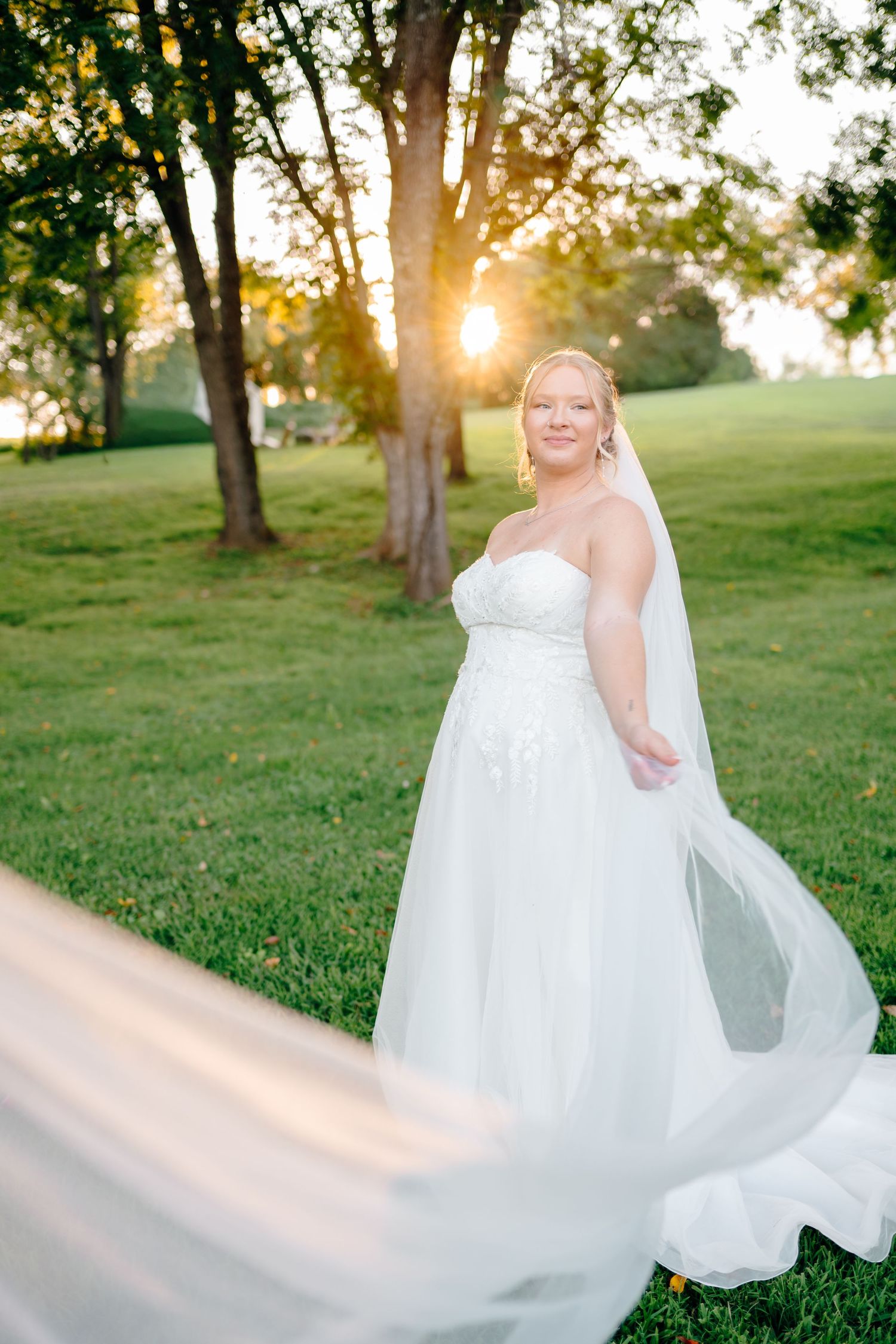 Flowing white wedding dress twirling in golden sunset light on grass.