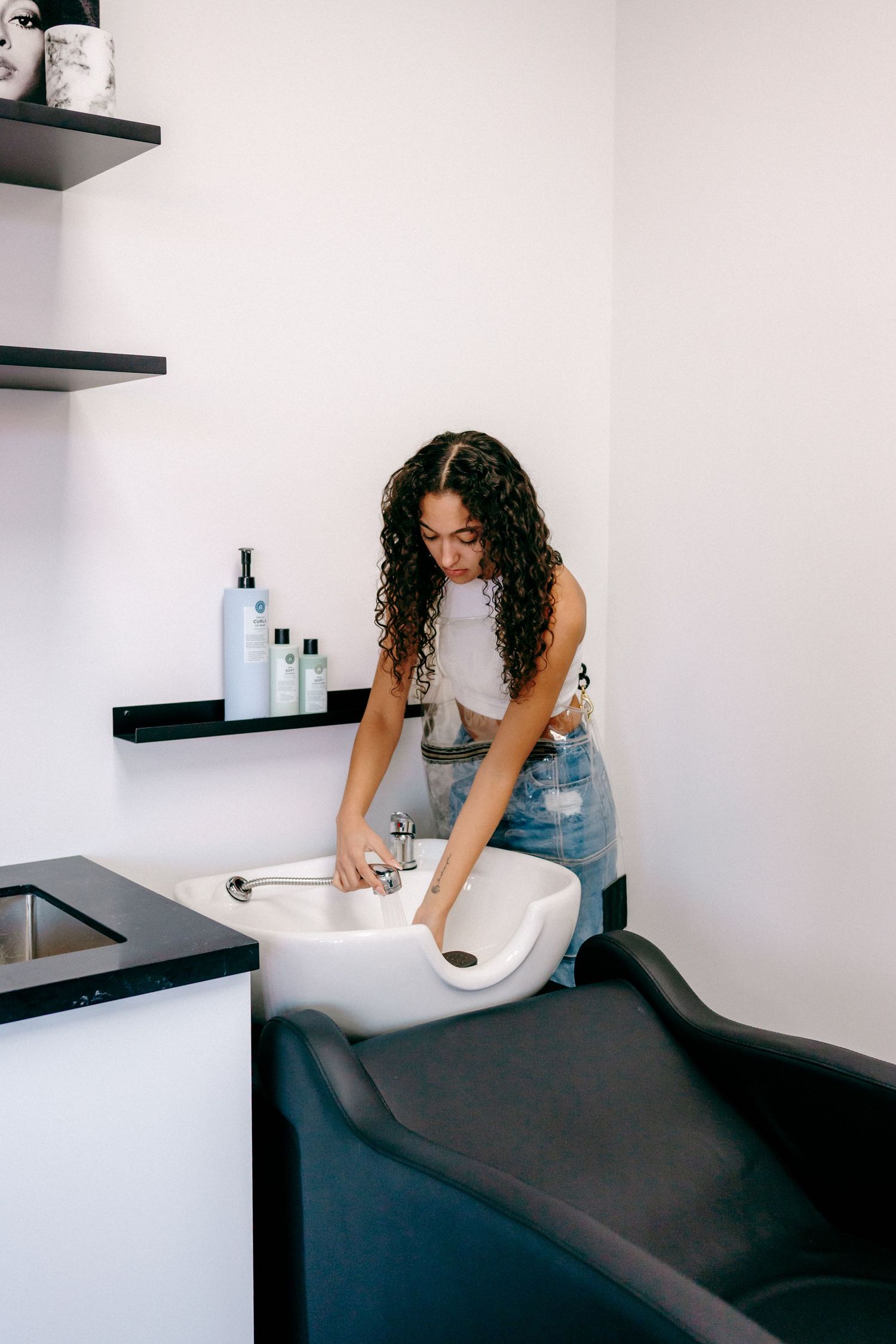 Person in pink top and jeans working at a salon wash basin.