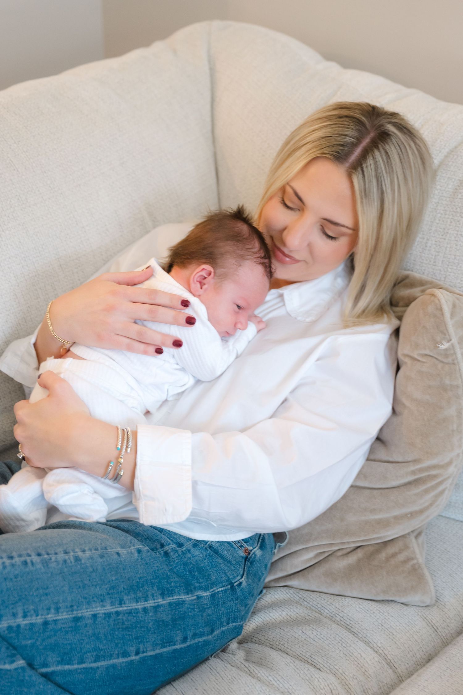 Tender moment of parent and baby resting together on gray couch.