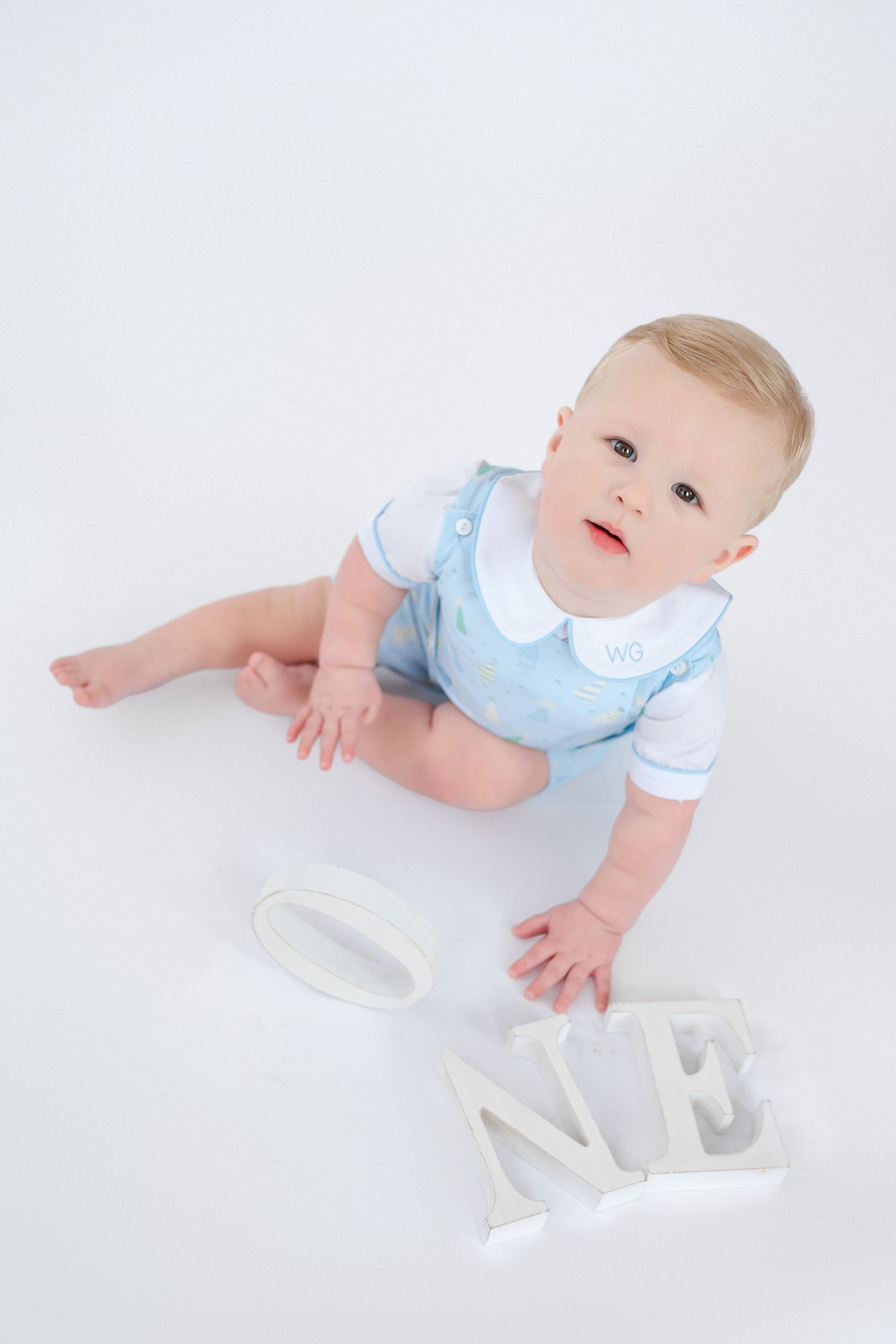 Baby wearing light blue bib crawls on white surface while reaching for letters in a series of photos.