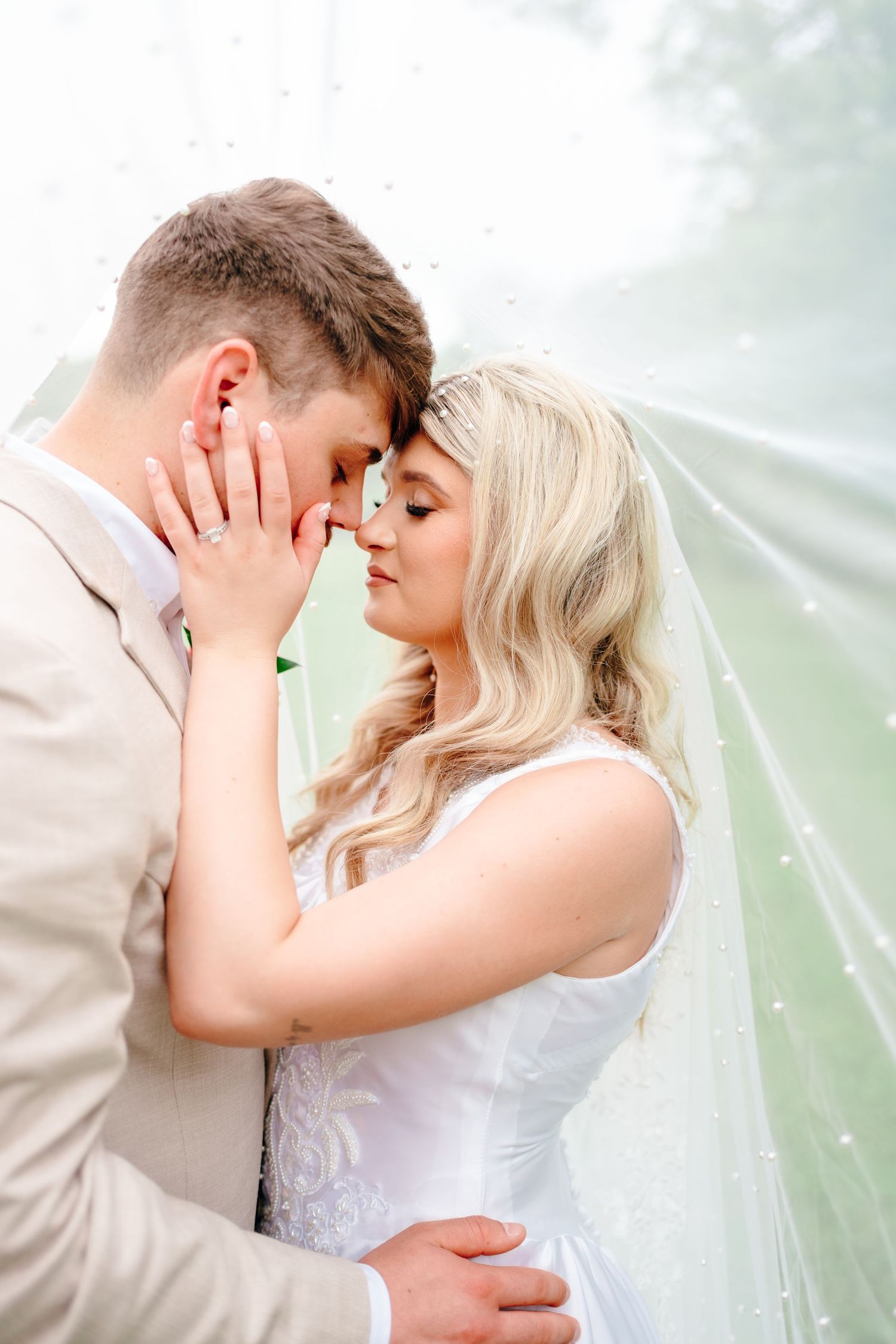 Romantic wedding couple shares intimate moments through flowing white veil.