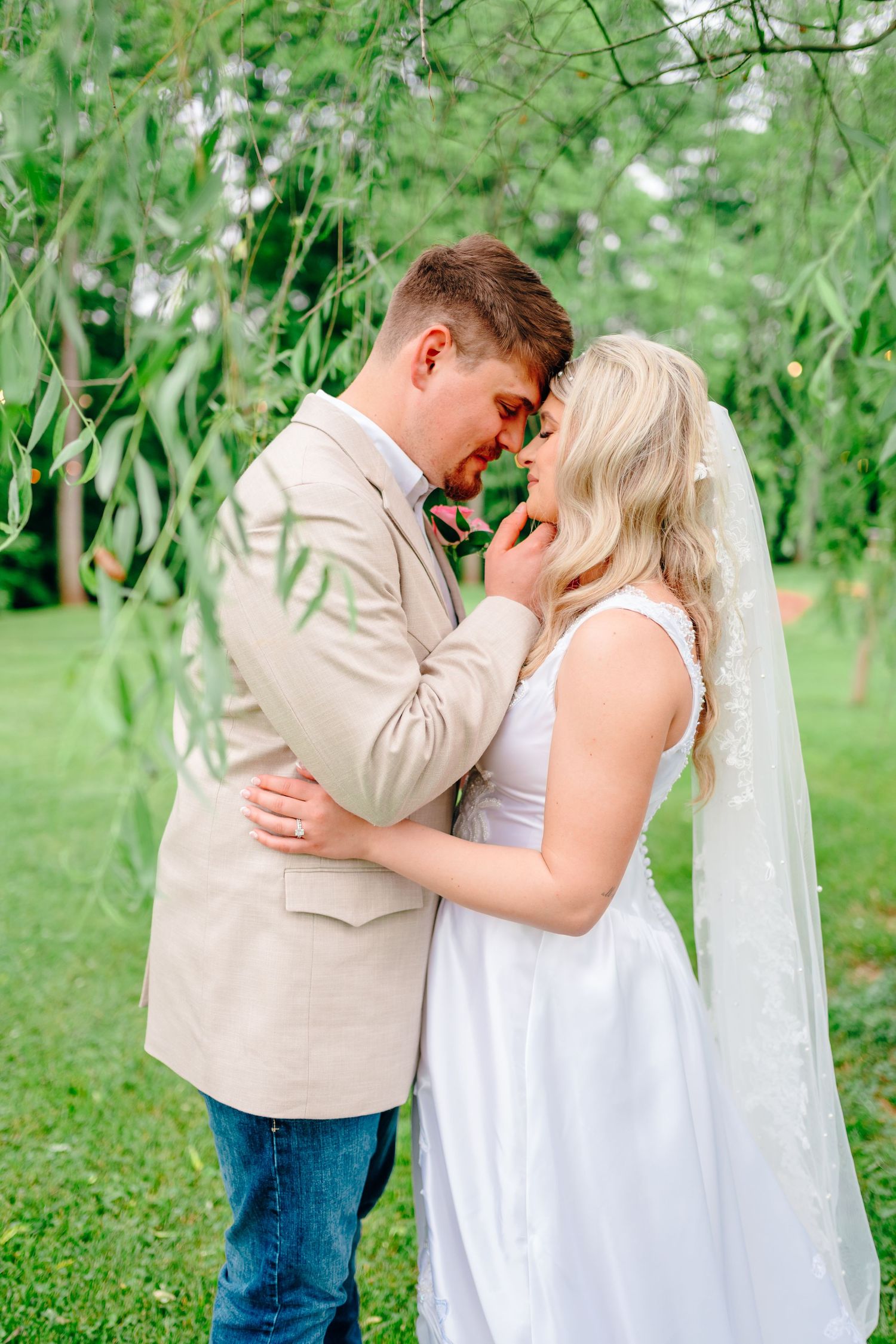Romantic outdoor wedding photos with couple embracing under green willow trees.