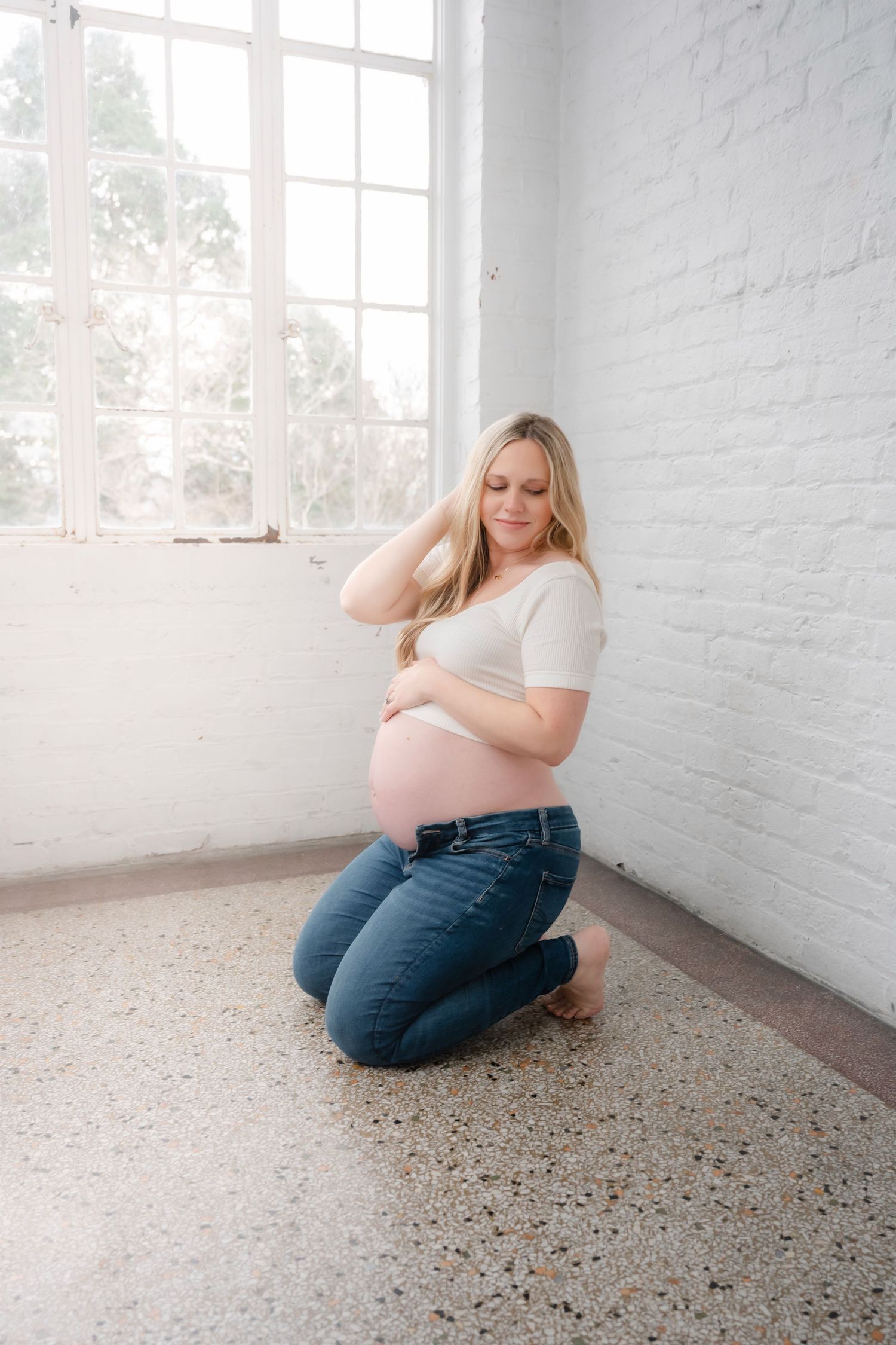 Artistic maternity portraits in bright white room with terrazzo flooring.