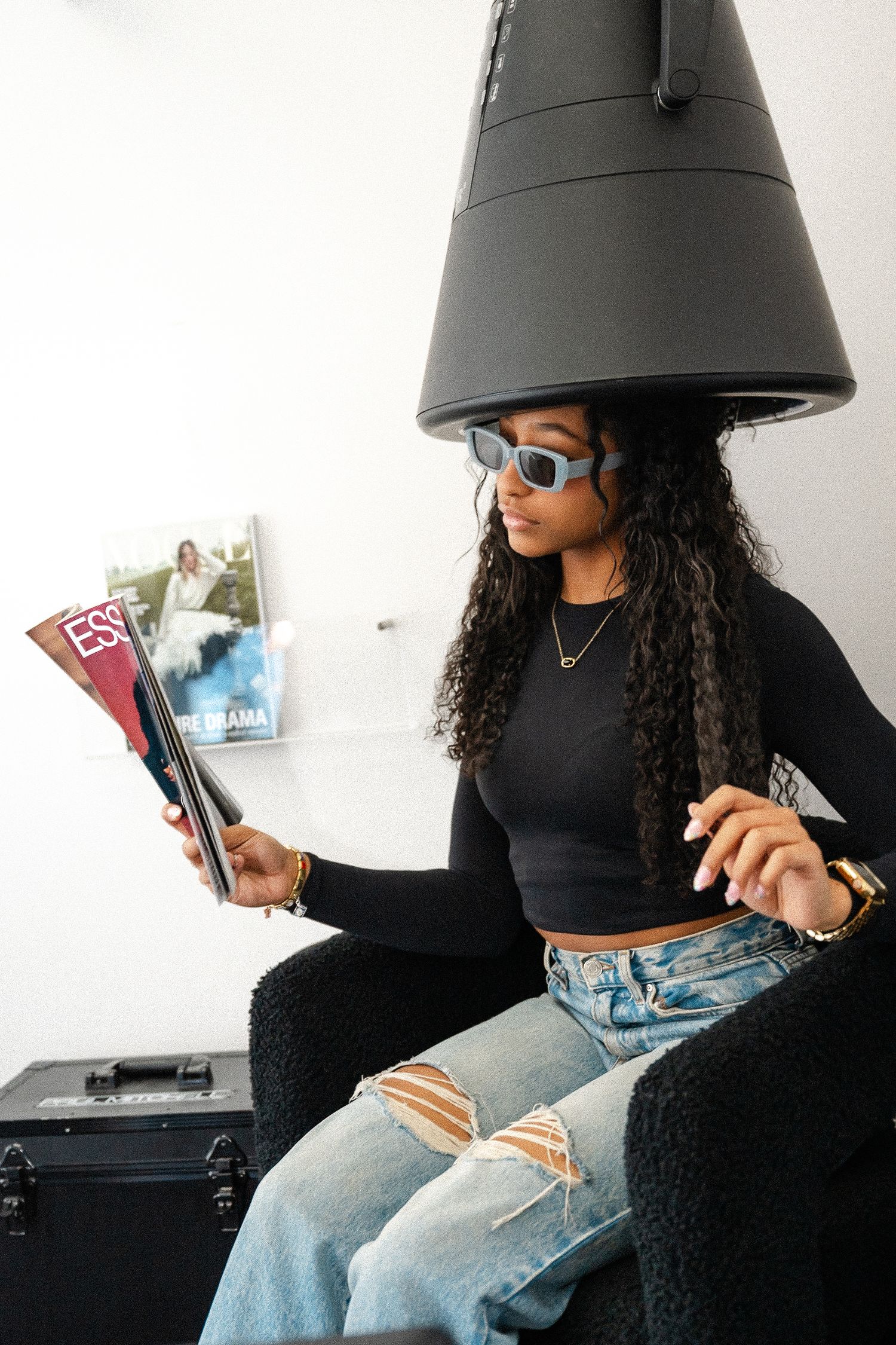 Stylish woman in sunglasses and black top reading magazines while sitting under a large pendant lamp.