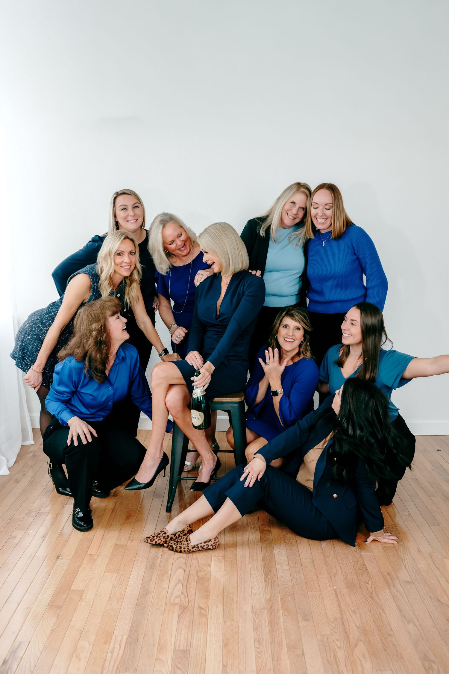 A group of friends in coordinating blue outfits laughing together on a hardwood floor during a casual photo session.