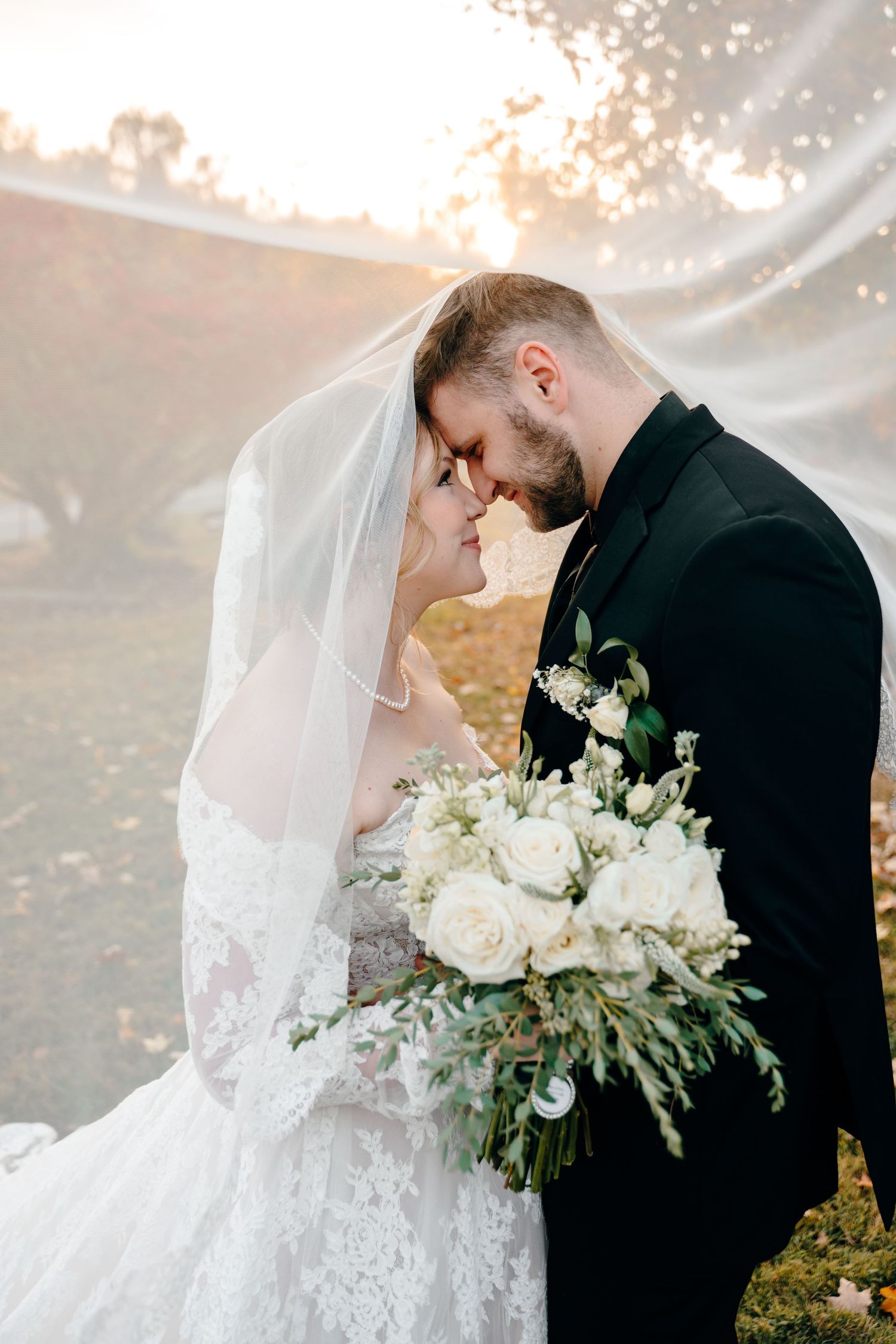 Intimate wedding portrait with flowing veil in golden autumn sunlight.