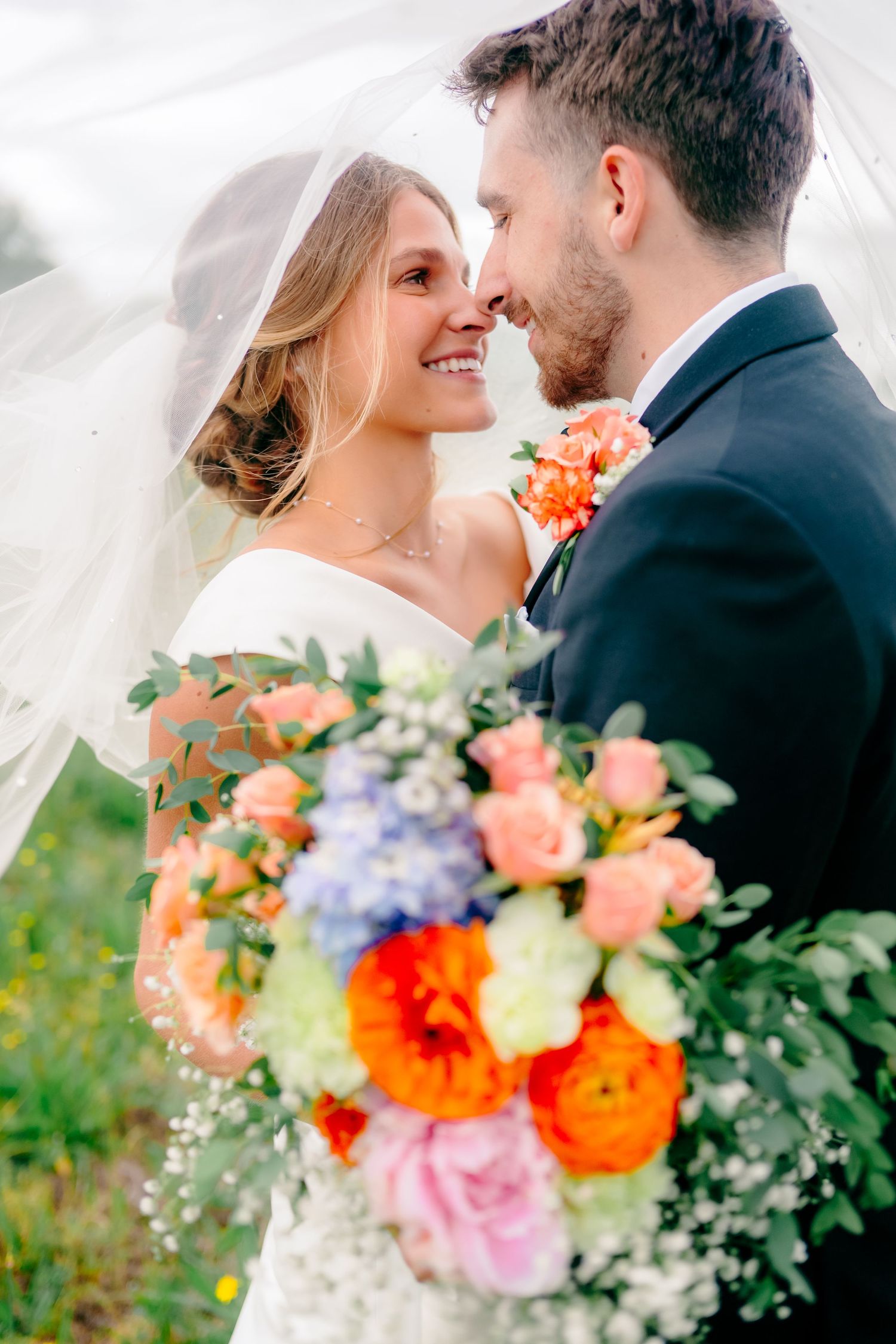 Romantic wedding portrait with vibrant coral and purple floral bouquet.