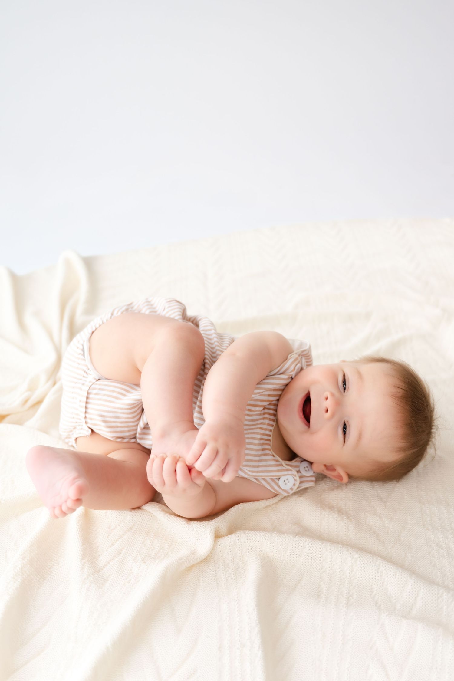 Baby in striped onesie lying on white blanket showing different playful poses.