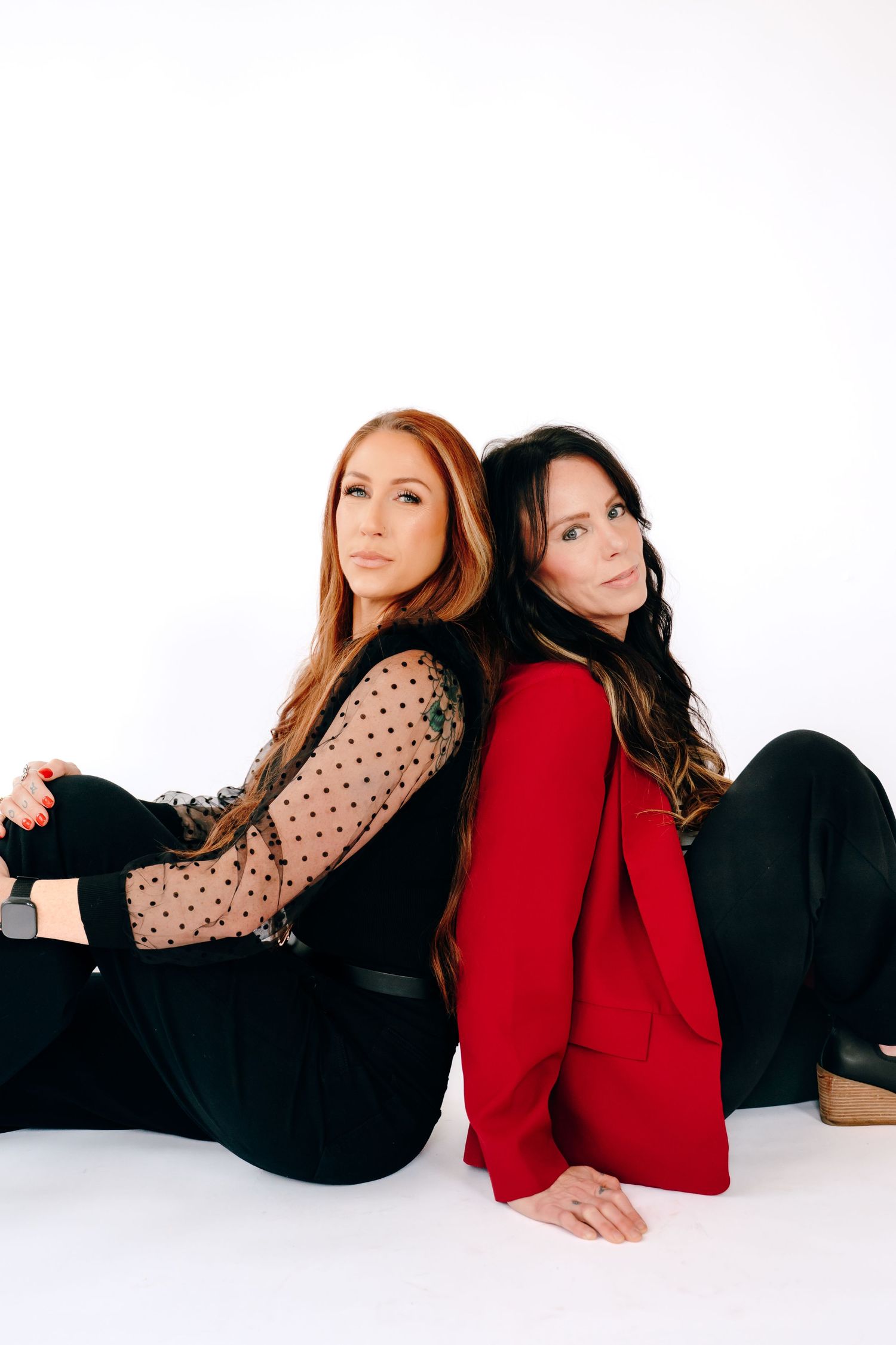 Two women in contrasting outfits pose together on a white background in a stylish fashion photo series.
