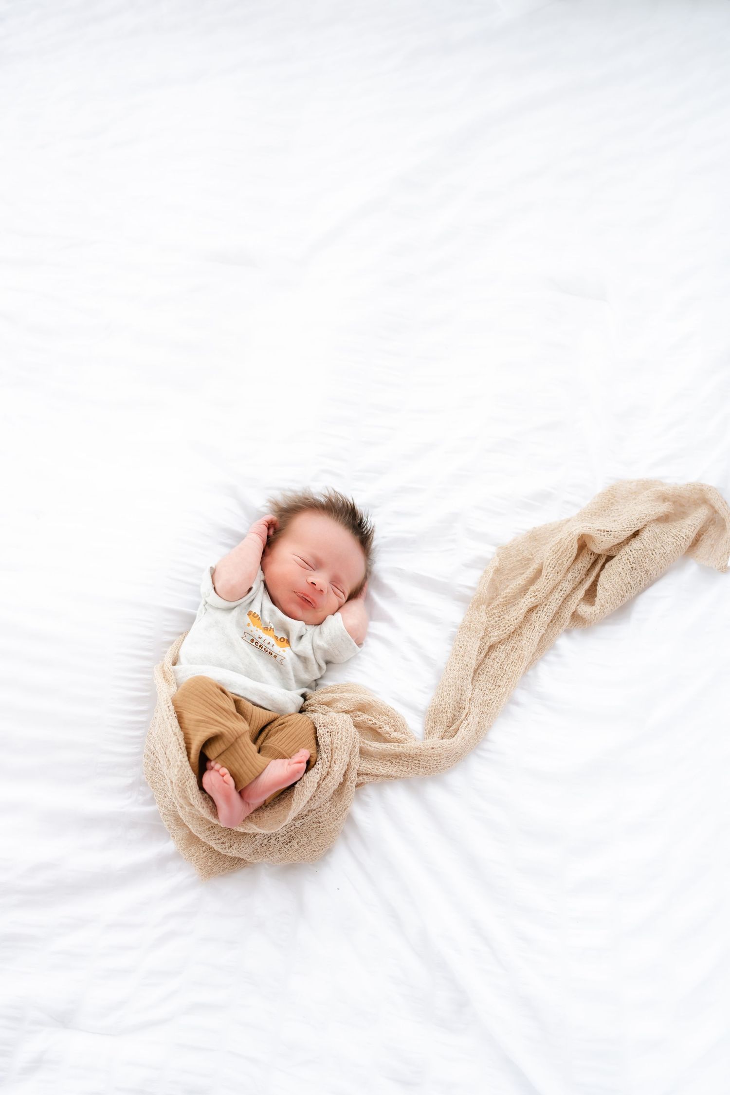 Sleeping newborn baby wrapped in soft beige knit blanket on white background.