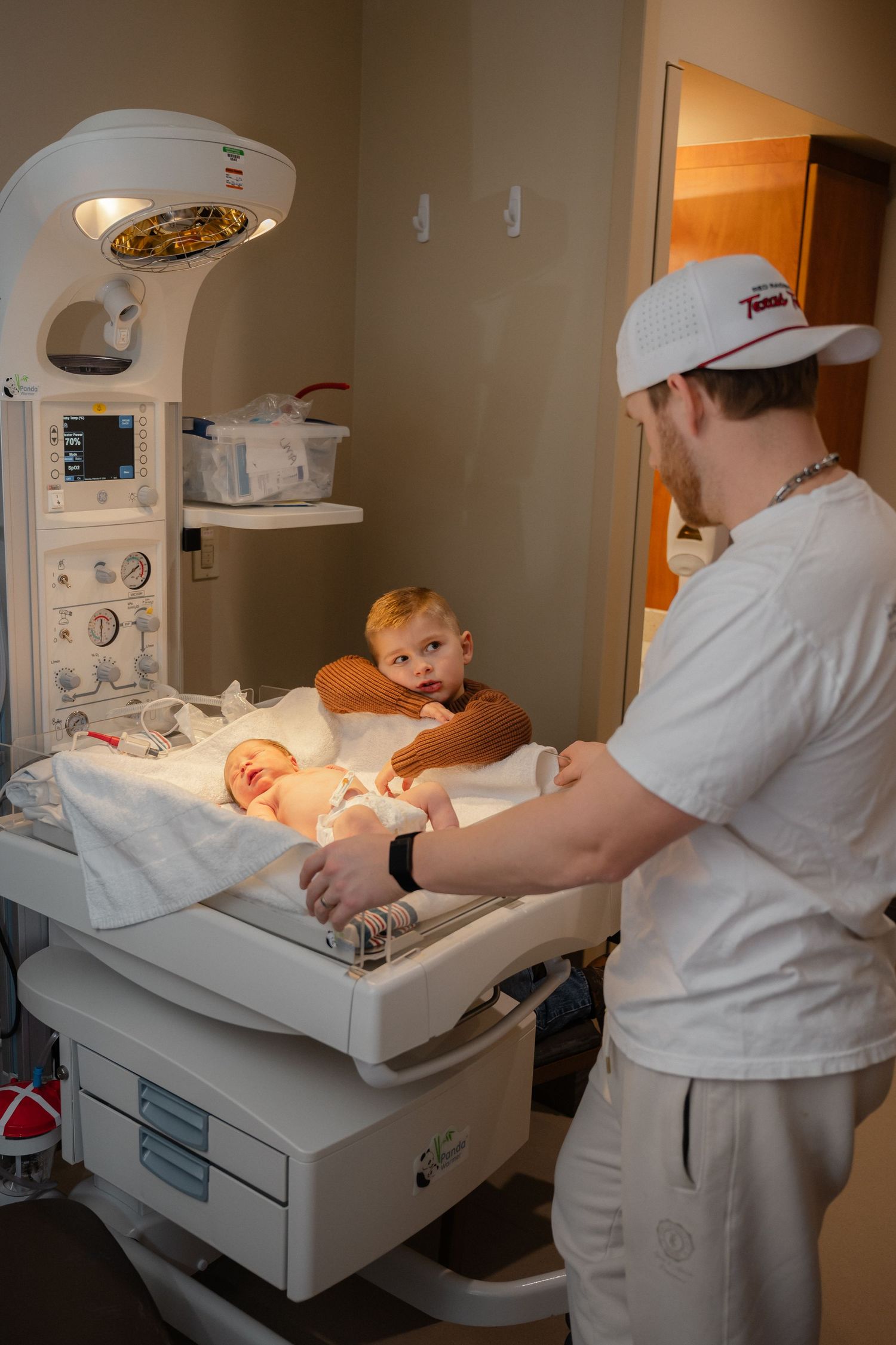 Medical staff in white uniforms examining newborn baby on hospital examination table.