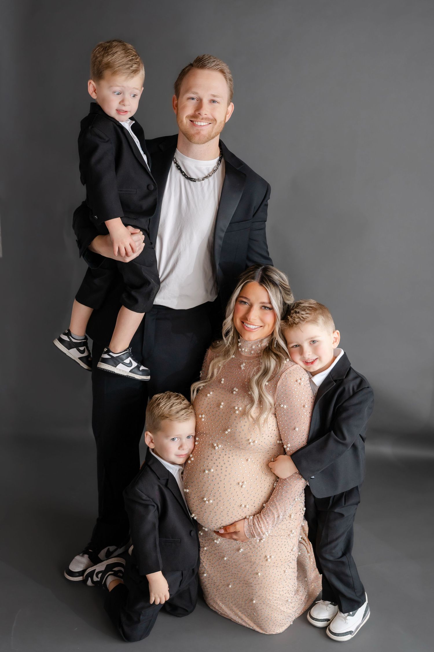 Studio family portrait with pregnant mother in beige dress surrounded by loved ones.