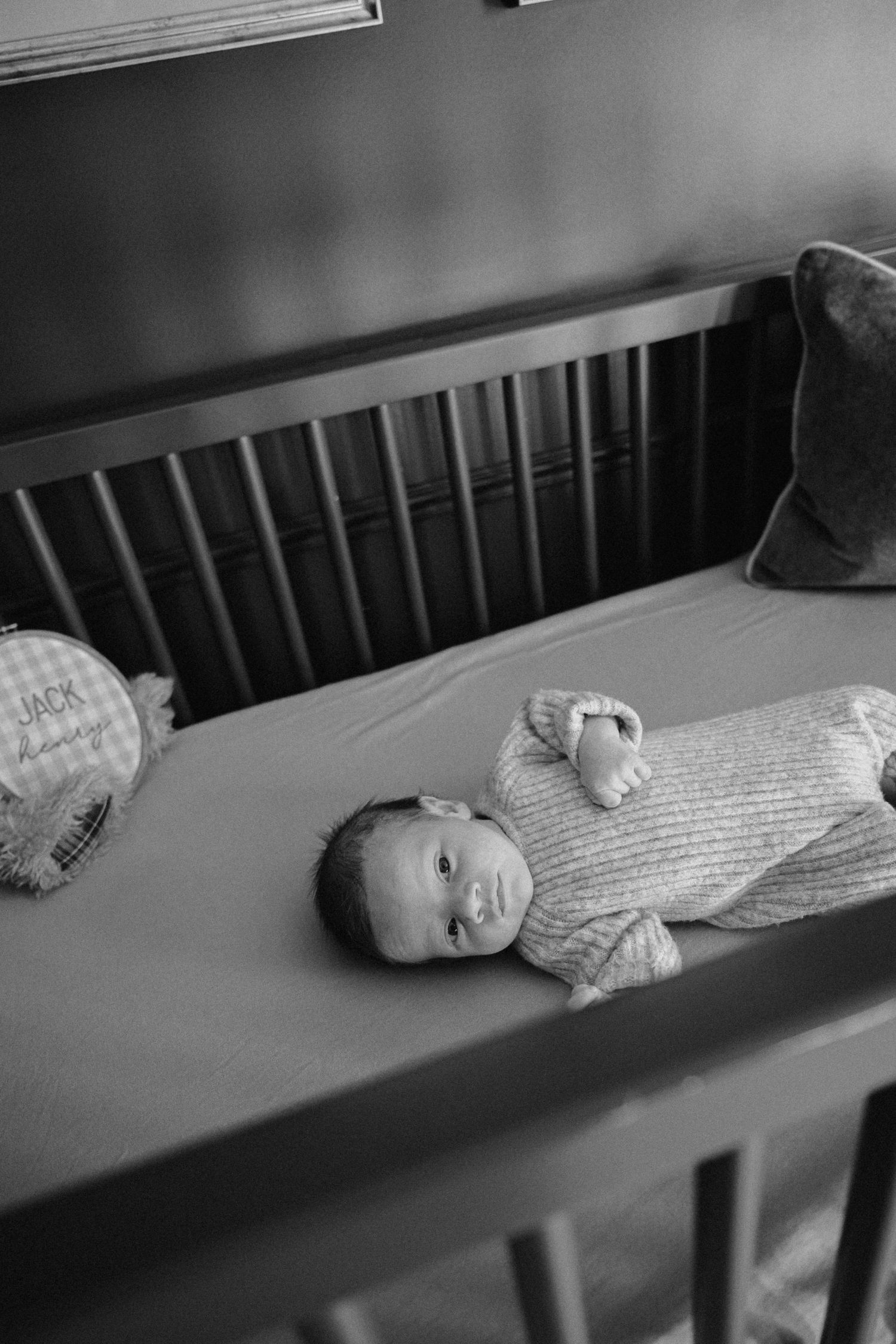 Black and white images of a baby lying in a crib looking peaceful.