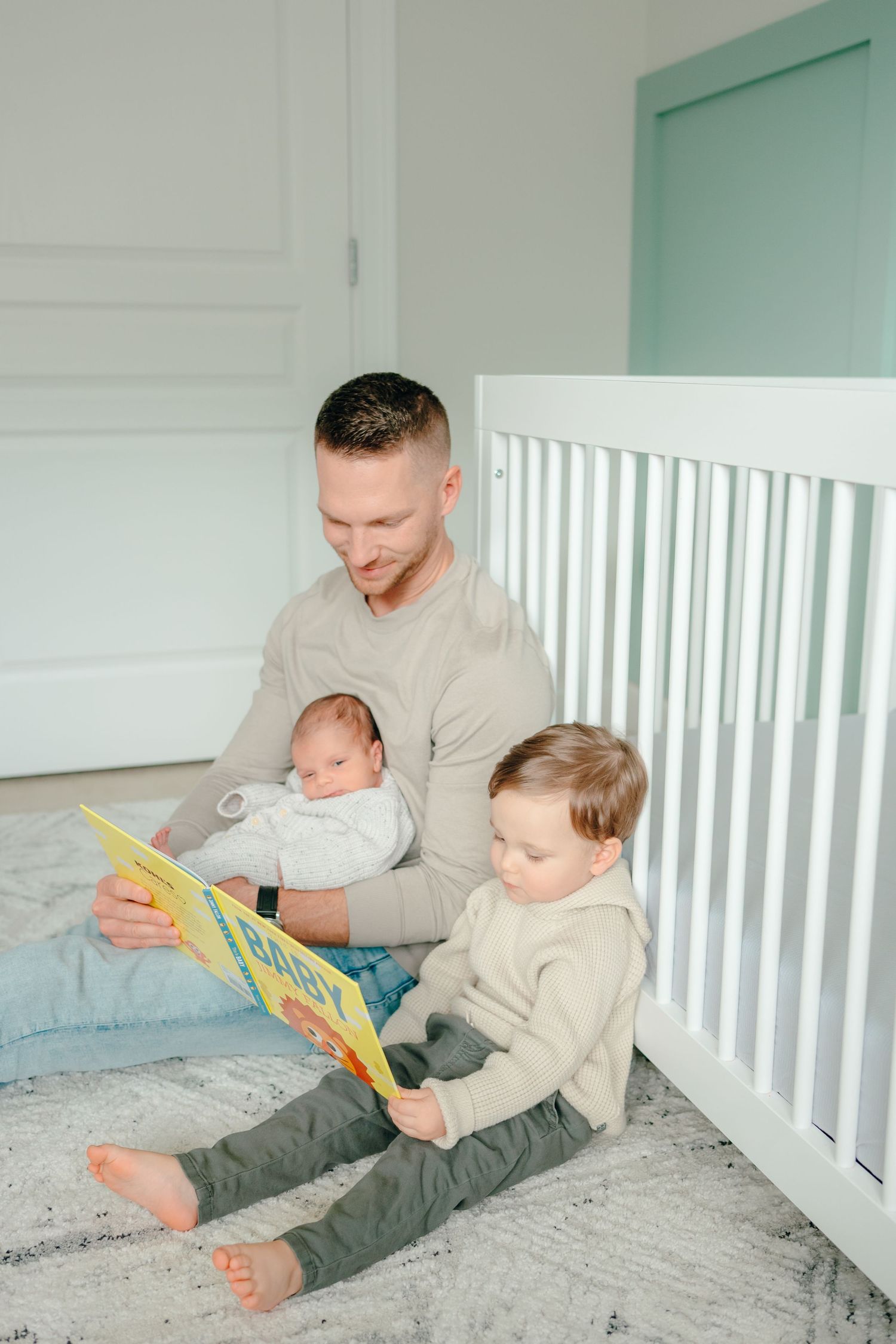 Father reads storybook to children while sitting in white crib.