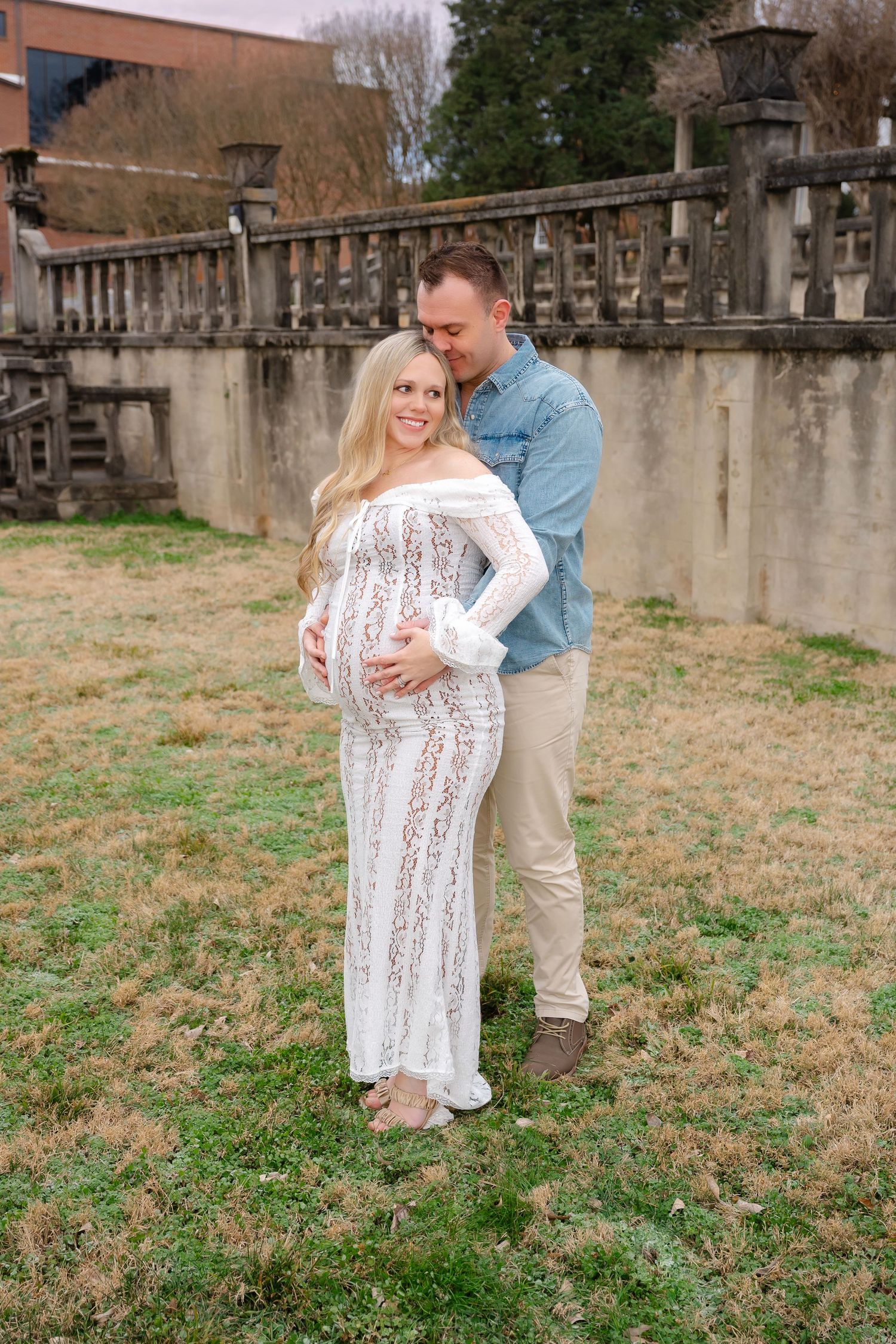 Couple embraces on grassy field near stone wall during outdoor photo session.