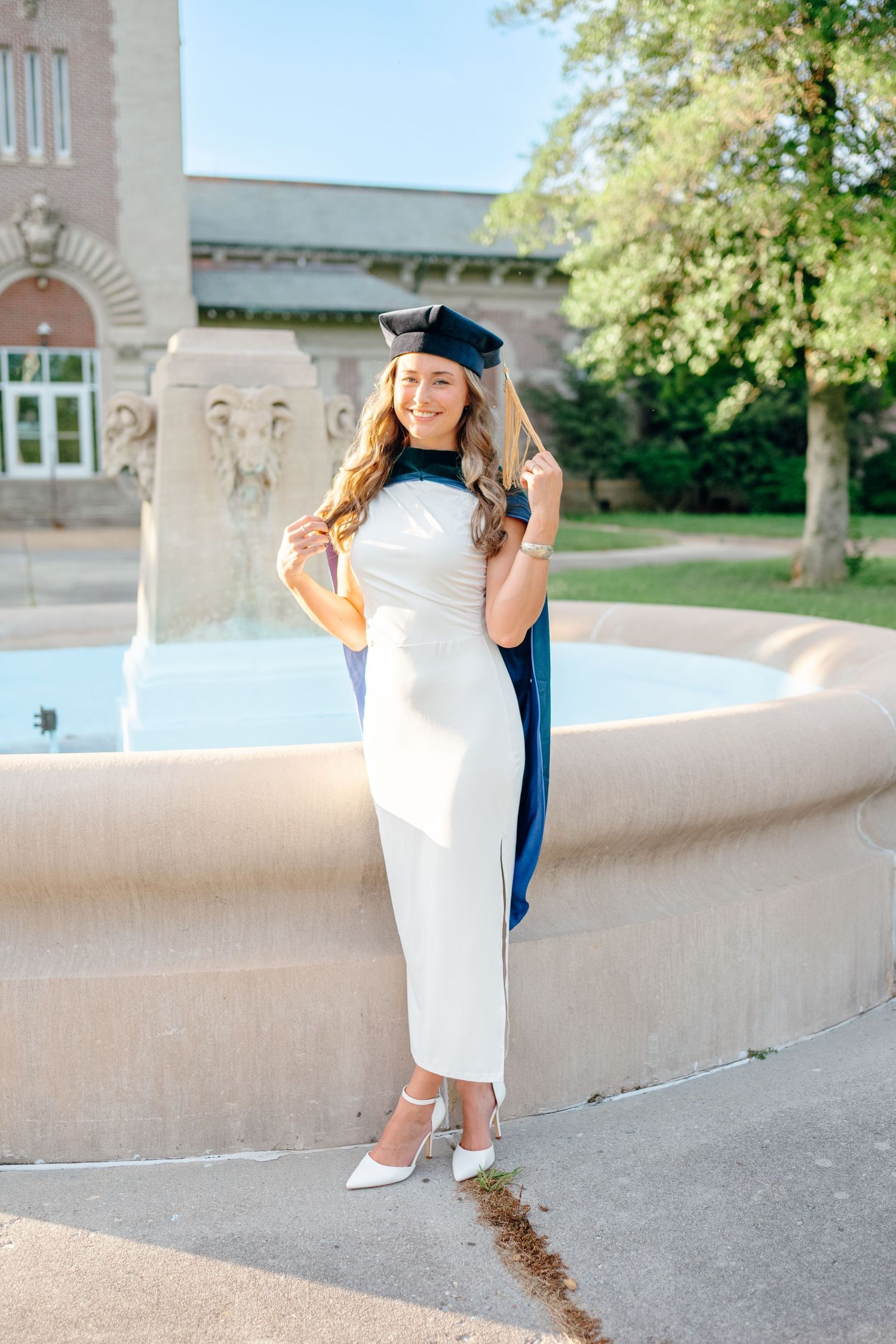 Celebratory graduation poses against campus architecture in white dress and blue regalia.