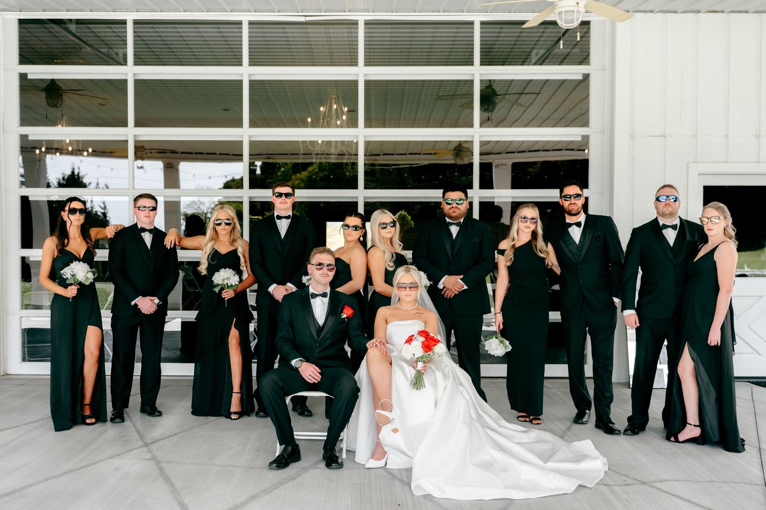 Wedding party lineup in black and white attire against modern glass building exterior.