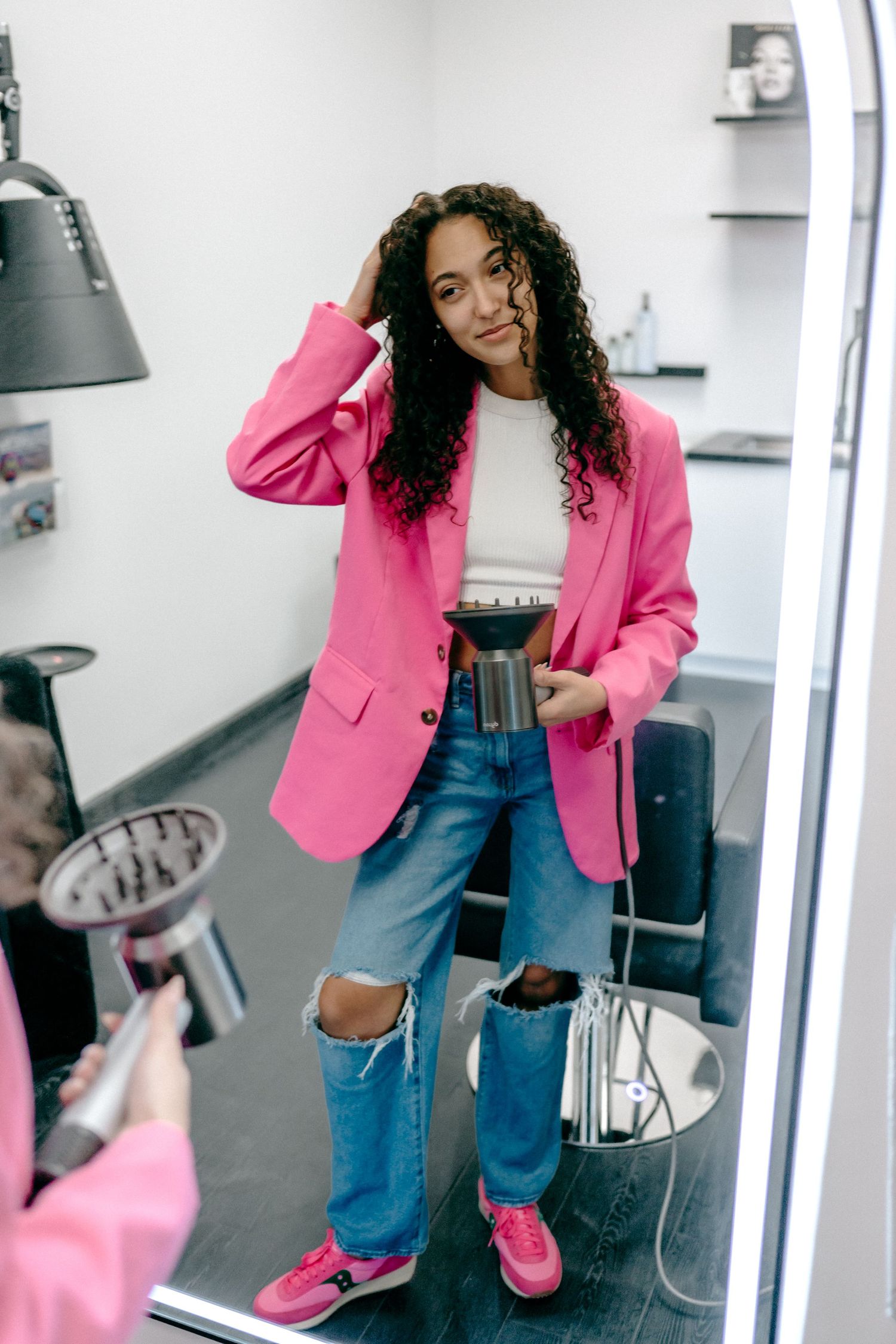 A trendy outfit featuring a bright pink blazer, ripped jeans and pink sneakers in a modern interior setting.
