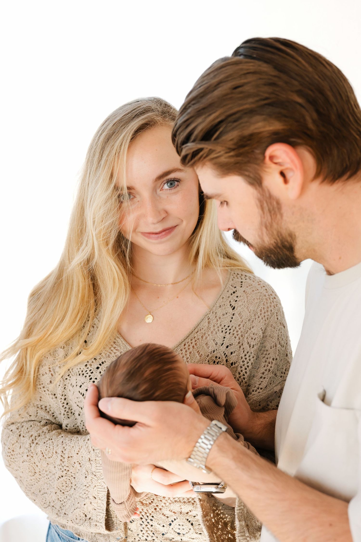 Young couple lovingly gazes at their newborn baby, mother in crochet top holding infant close.