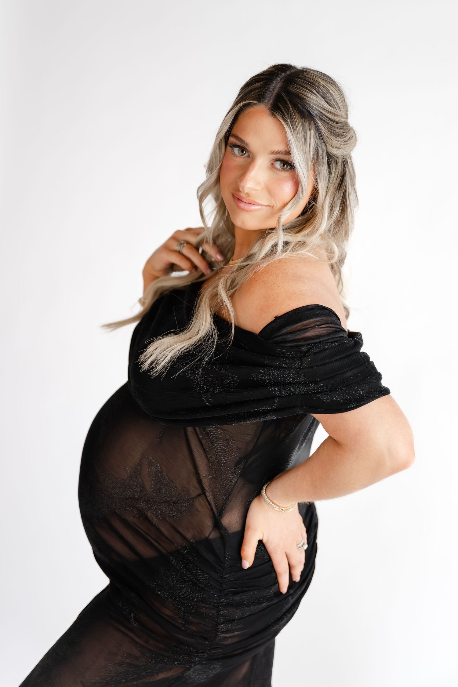 Artistic maternity portraits in a flowing black dress against white backdrop.
