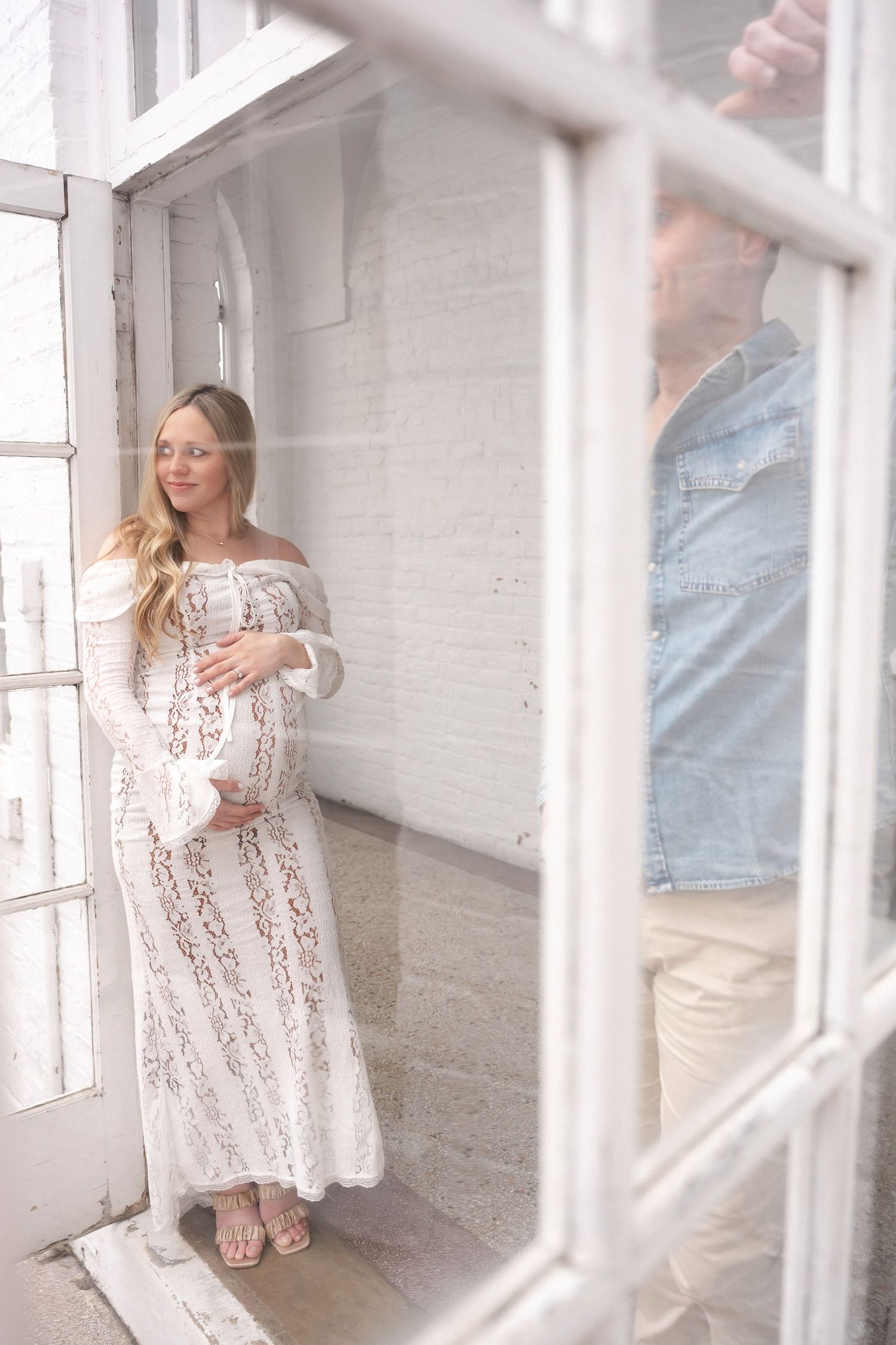 Woman in lace dress twirls through bright white room with large windows.