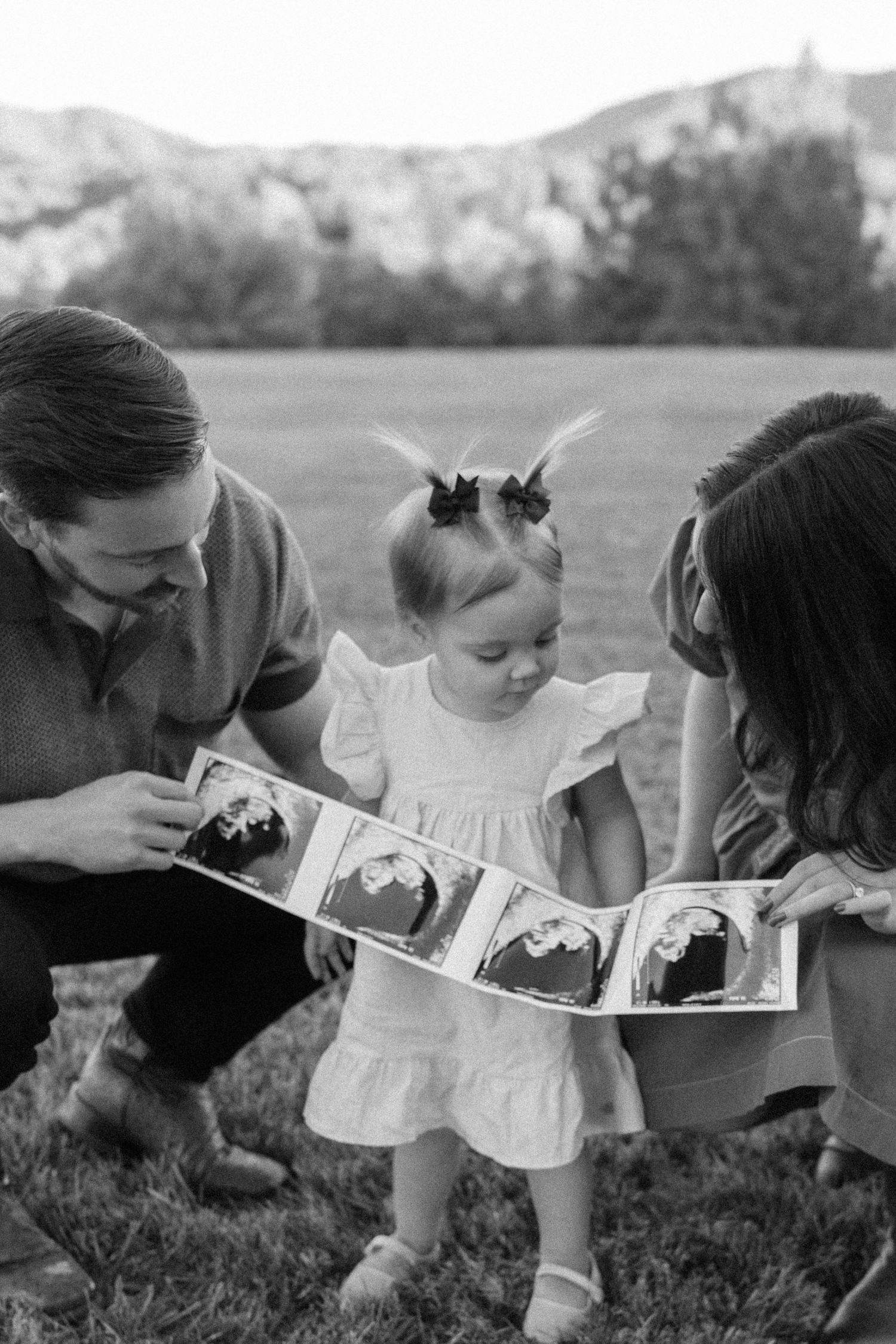 A family looks at ultrasound photos together while sitting in a grassy field.