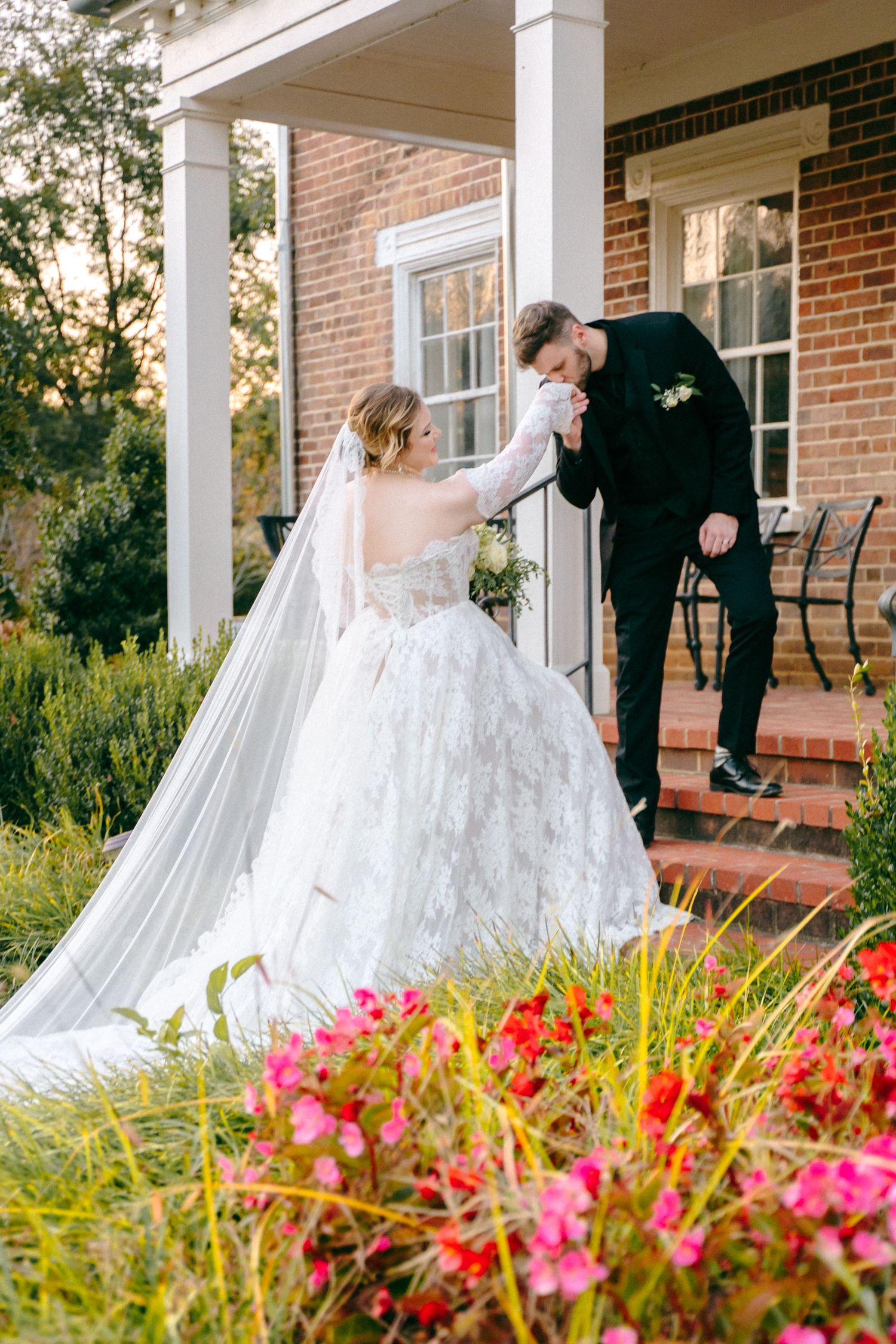 Wedding couple on porch with flowing dress and colorful garden flowers in foreground.