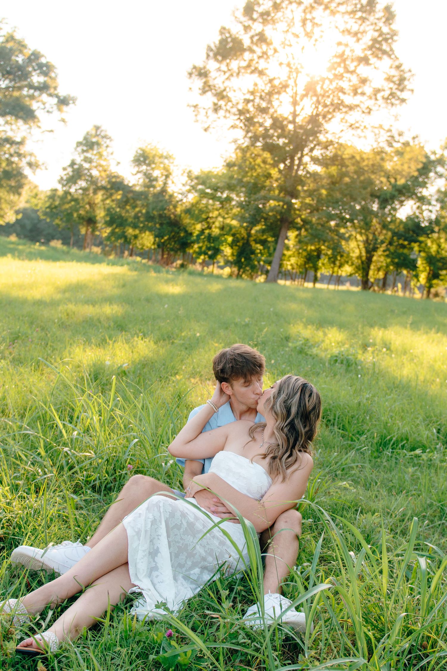 A couple shares an intimate moment while lying in tall grass during golden hour.
