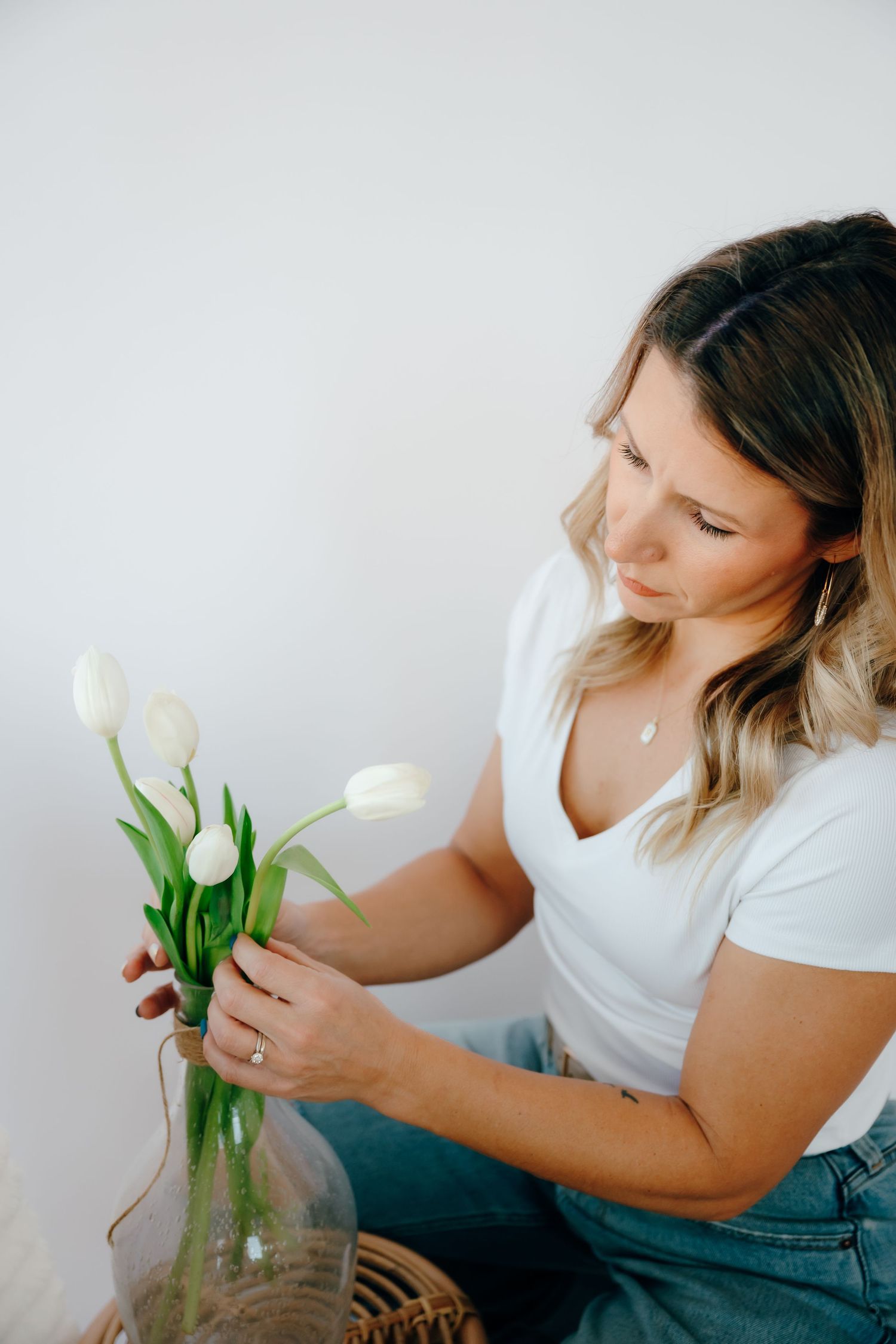 A series of images showing someone arranging white tulips in a clear glass vase against a white background.