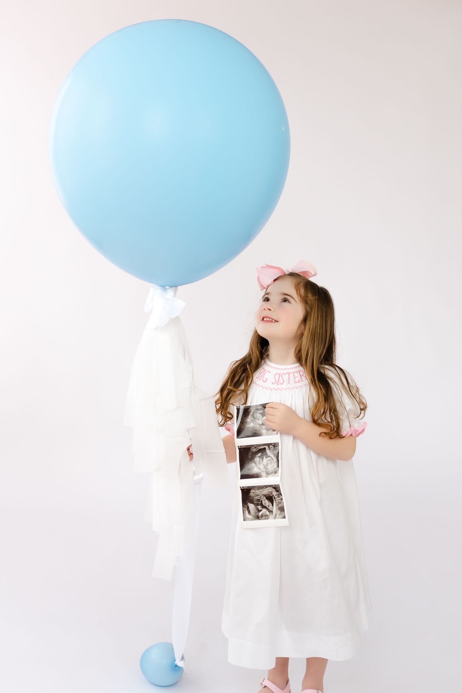 Creative pregnancy announcement photo series with white dress and large blue balloon against light background.