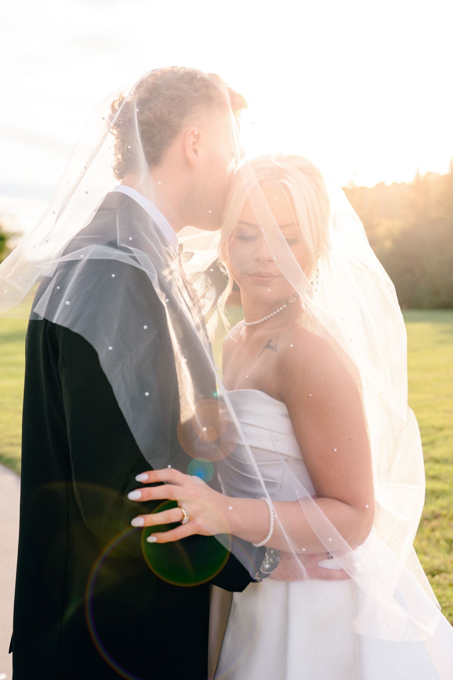 Intimate wedding moment captured in golden sunlight through bride's veil.